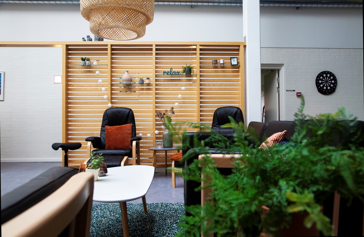 Skillevæggen i dagligstuen med sorte sofaer og sorte lænestole hvidt sofabord og en stor grøn plante