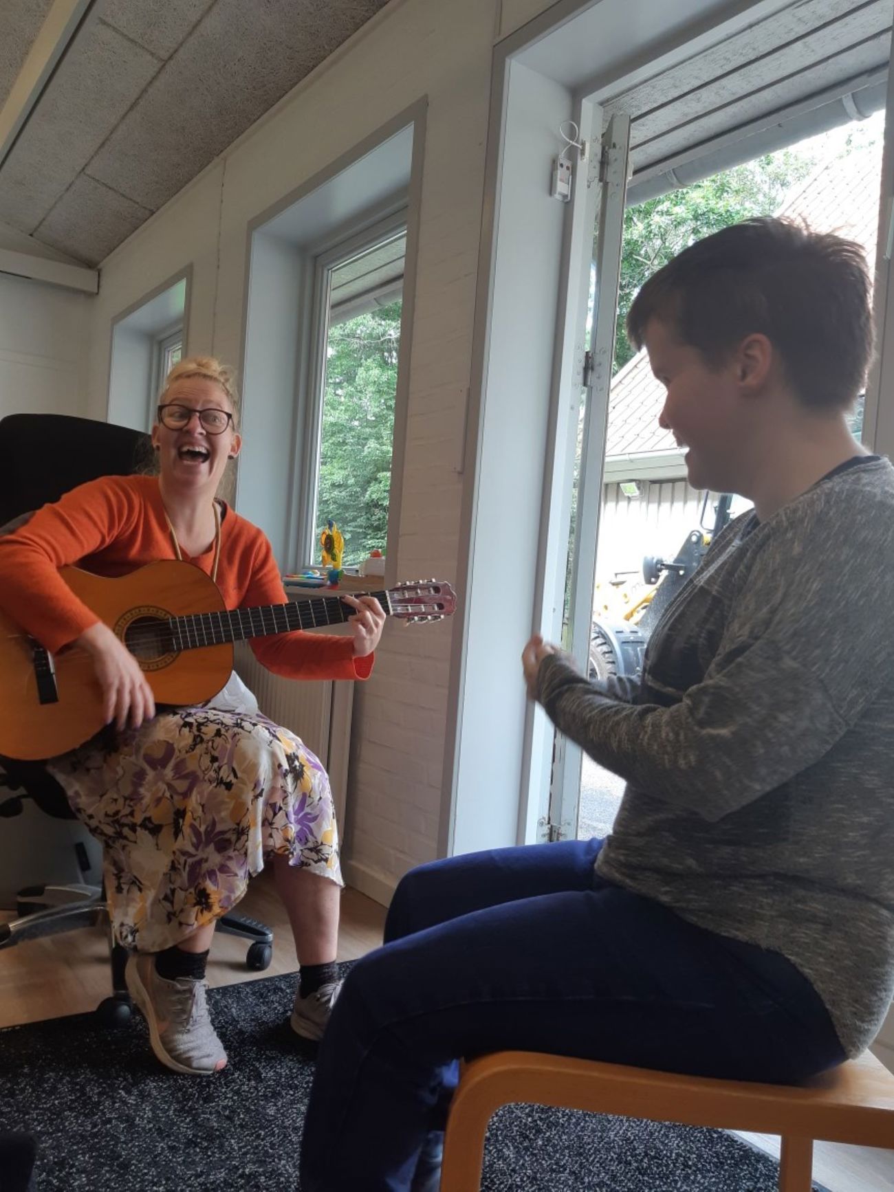 En borger og en pædagog, pædagogen spiller på guitar og synge til borgeren.