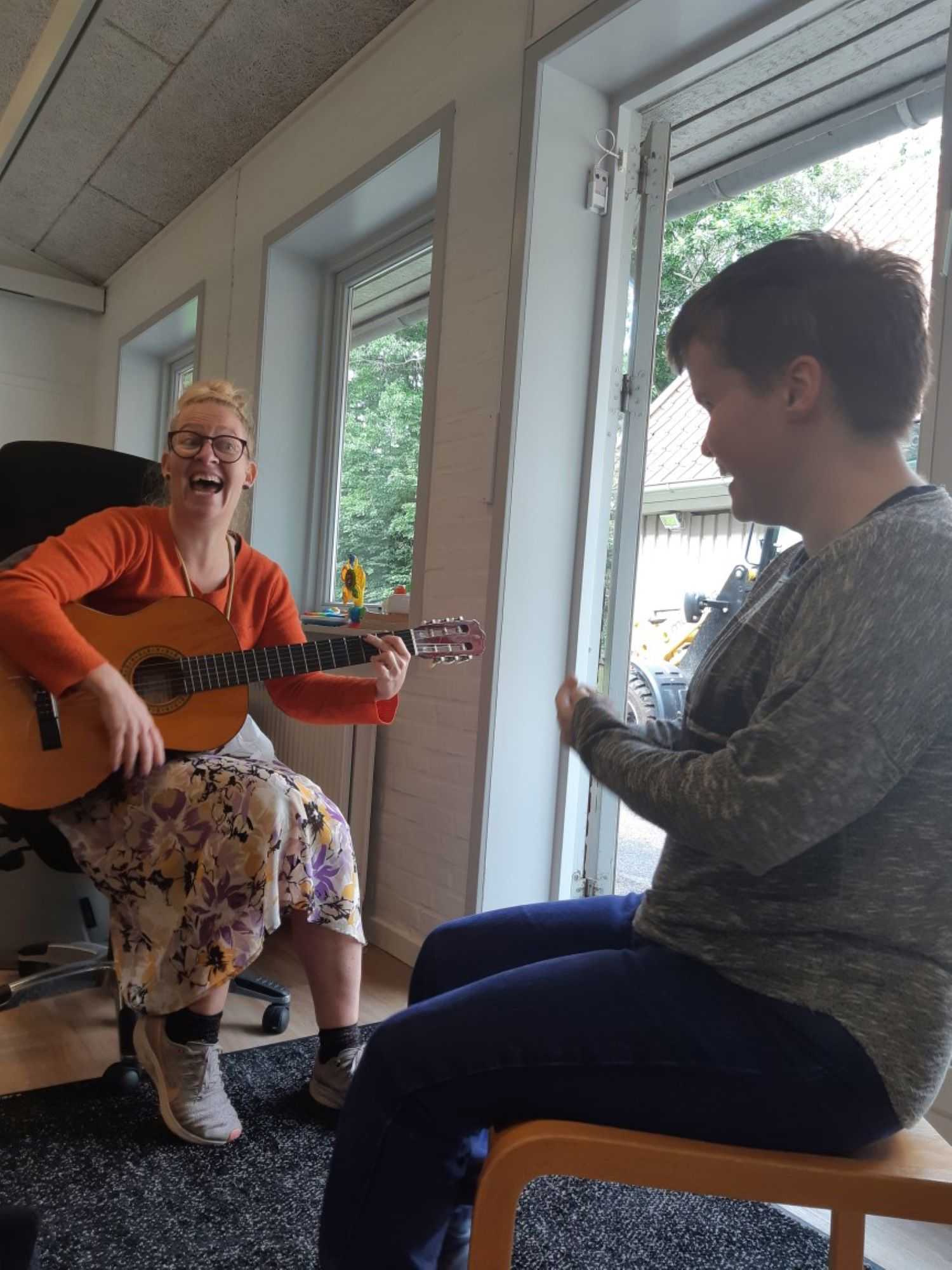 En borger og en pædagog, pædagogen spiller på guitar og synge til borgeren.