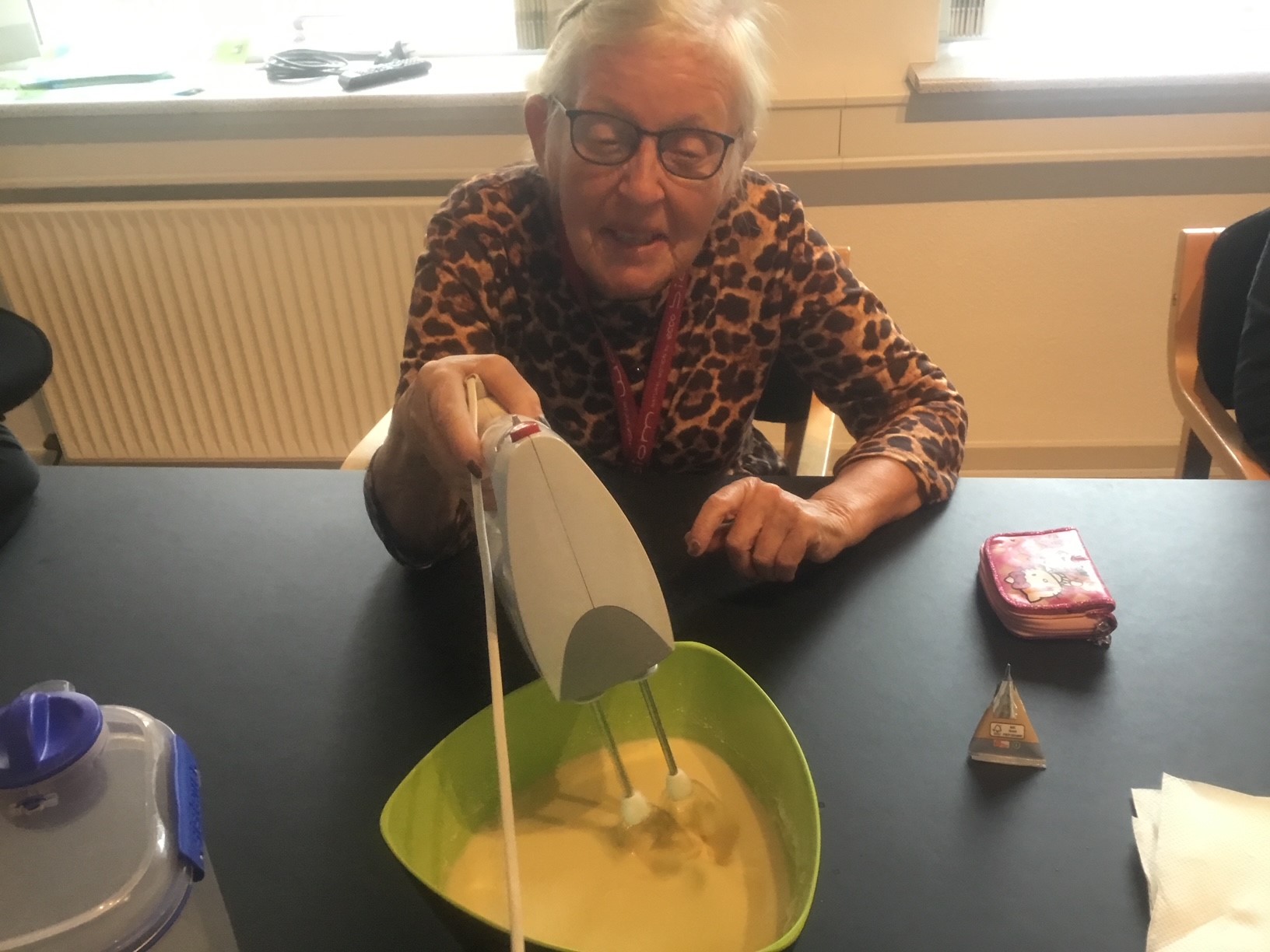 En borger er ved at piske noget hvidt i grøn skål, hun sidder ved et sort bord.