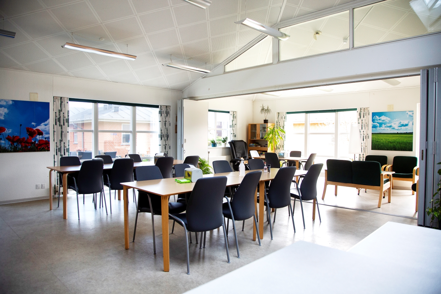 Fællesrum med spiseborde og stole, samt et opdelt rum med sofaer og lænestole man kan lukke af til.