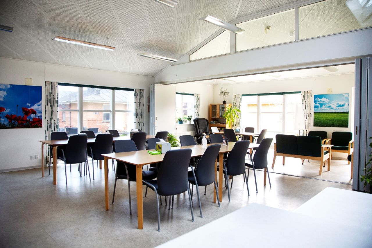 Fællesrum med spiseborde og stole, samt et opdelt rum med sofaer og lænestole man kan lukke af til.