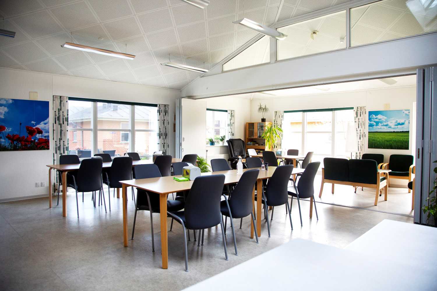 Fællesrum med spiseborde og stole, samt et opdelt rum med sofaer og lænestole man kan lukke af til.