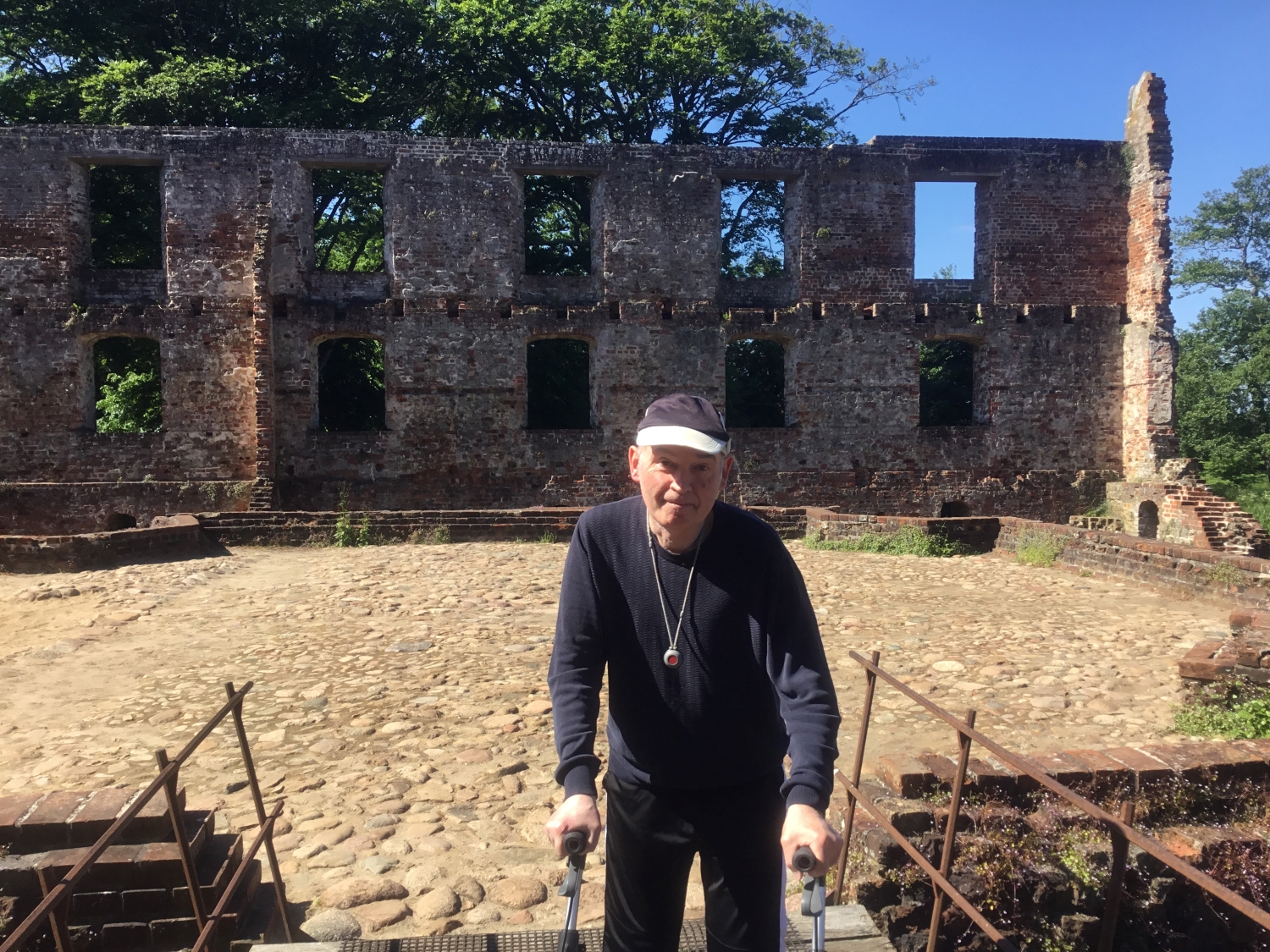 En borger ved Trøjborgslotsruin, i baggrunden ses ruinen i røde mursten, der er vinduer og gulvet er af store brosten, det er solskind og træerne er grønne 