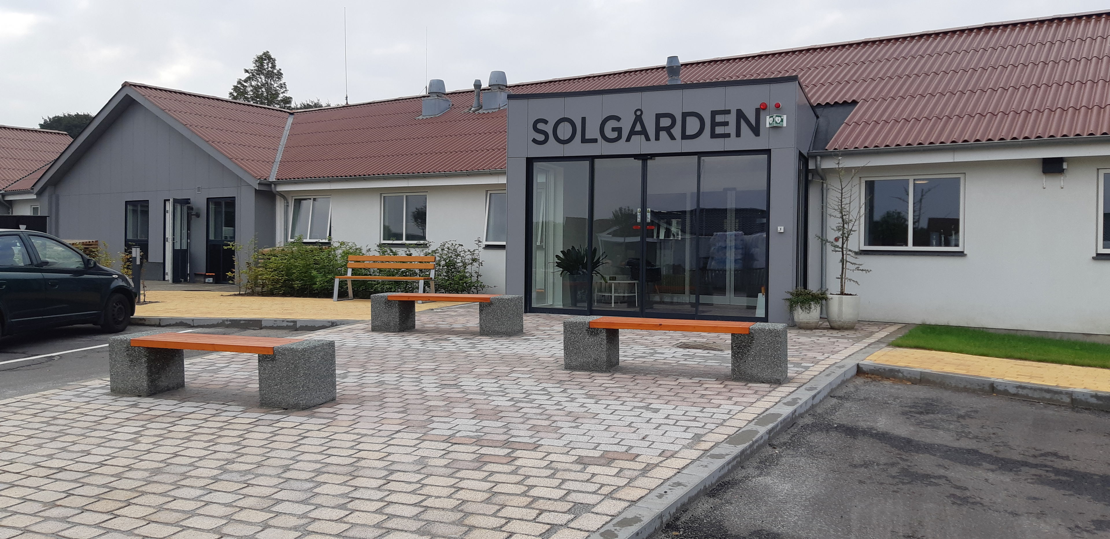 Forsiden af Solgården, grå fliser og nogle bænke i beton med træsæder