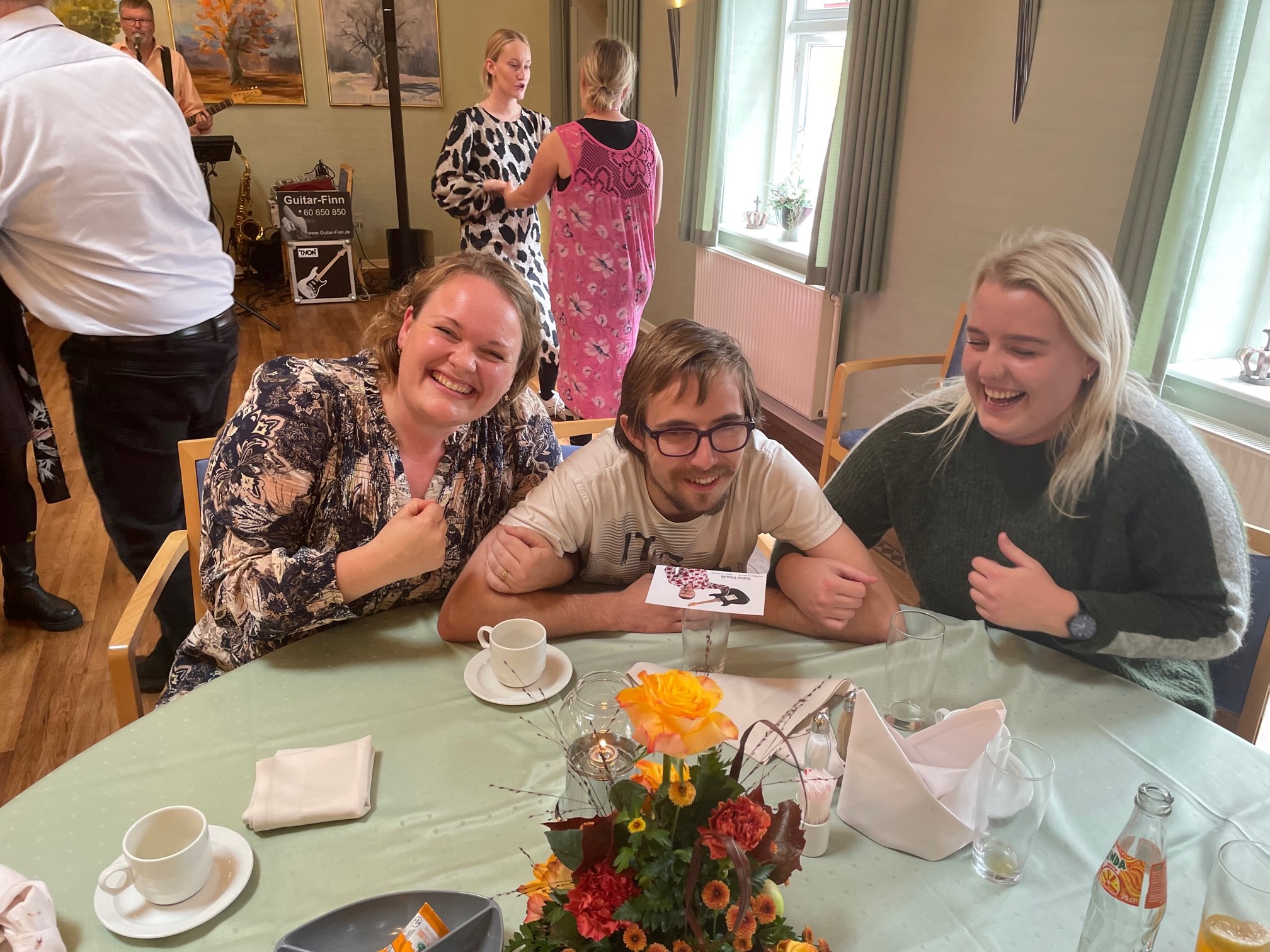 # glade gæster der smiler til cameraet, i baggrunden kan man se nogle der dansker til musikken