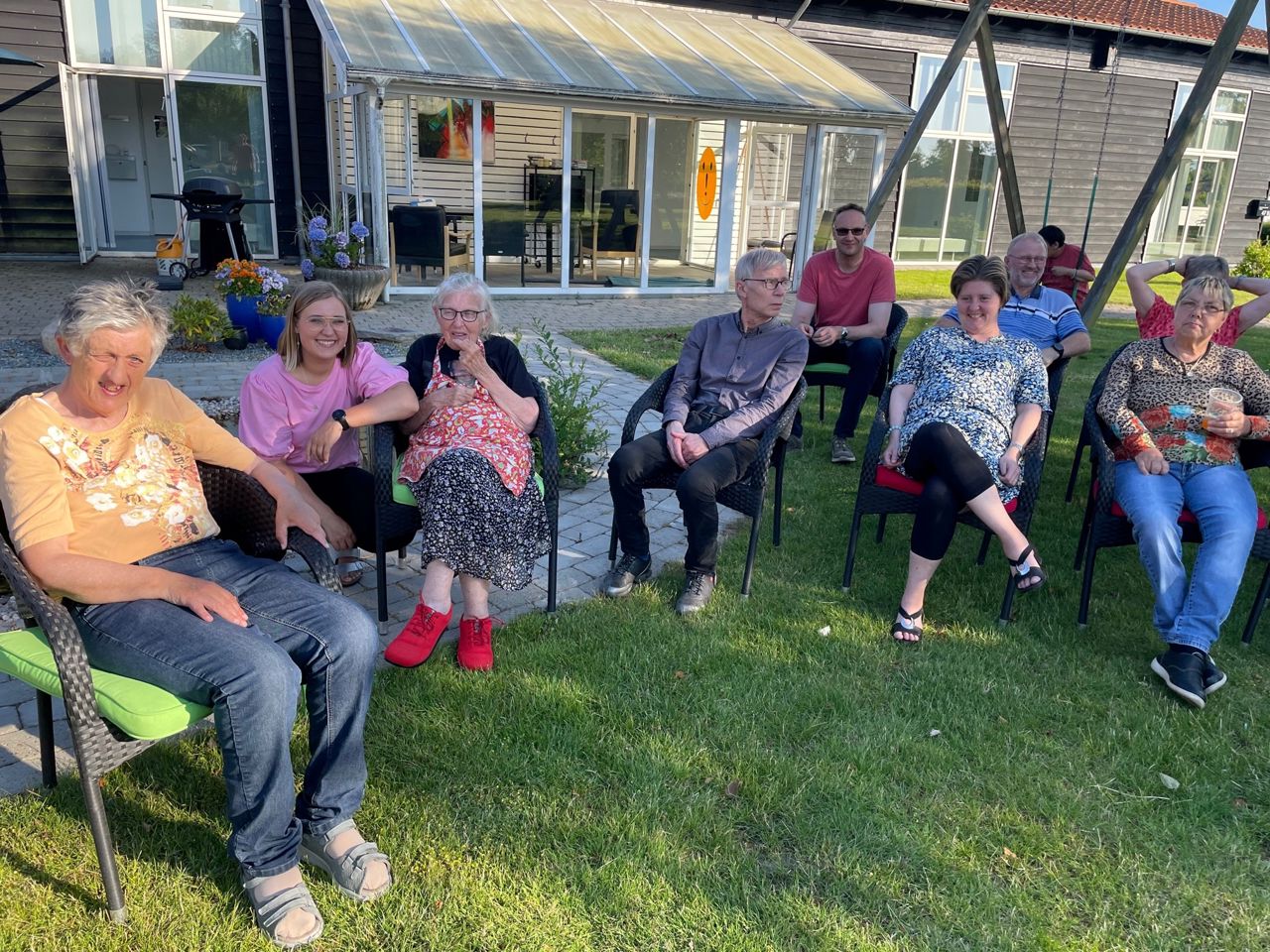 Borgerne sidder i halvcirkel på stole på græsplænen, det er godt vejr og nogle kniber øjnene sammen pga. solen.