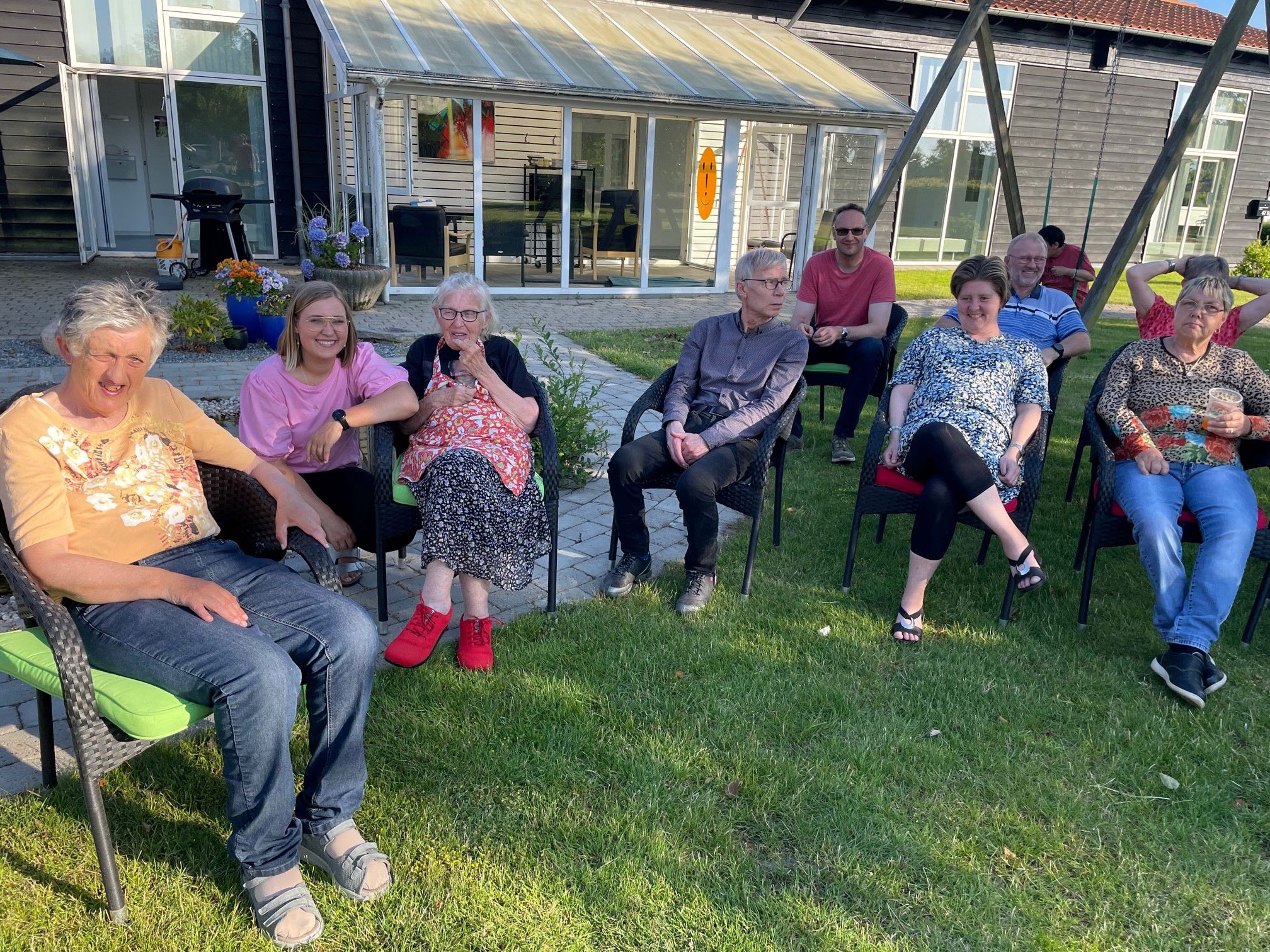 Borgerne sidder i halvcirkel på stole på græsplænen, det er godt vejr og nogle kniber øjnene sammen pga. solen.