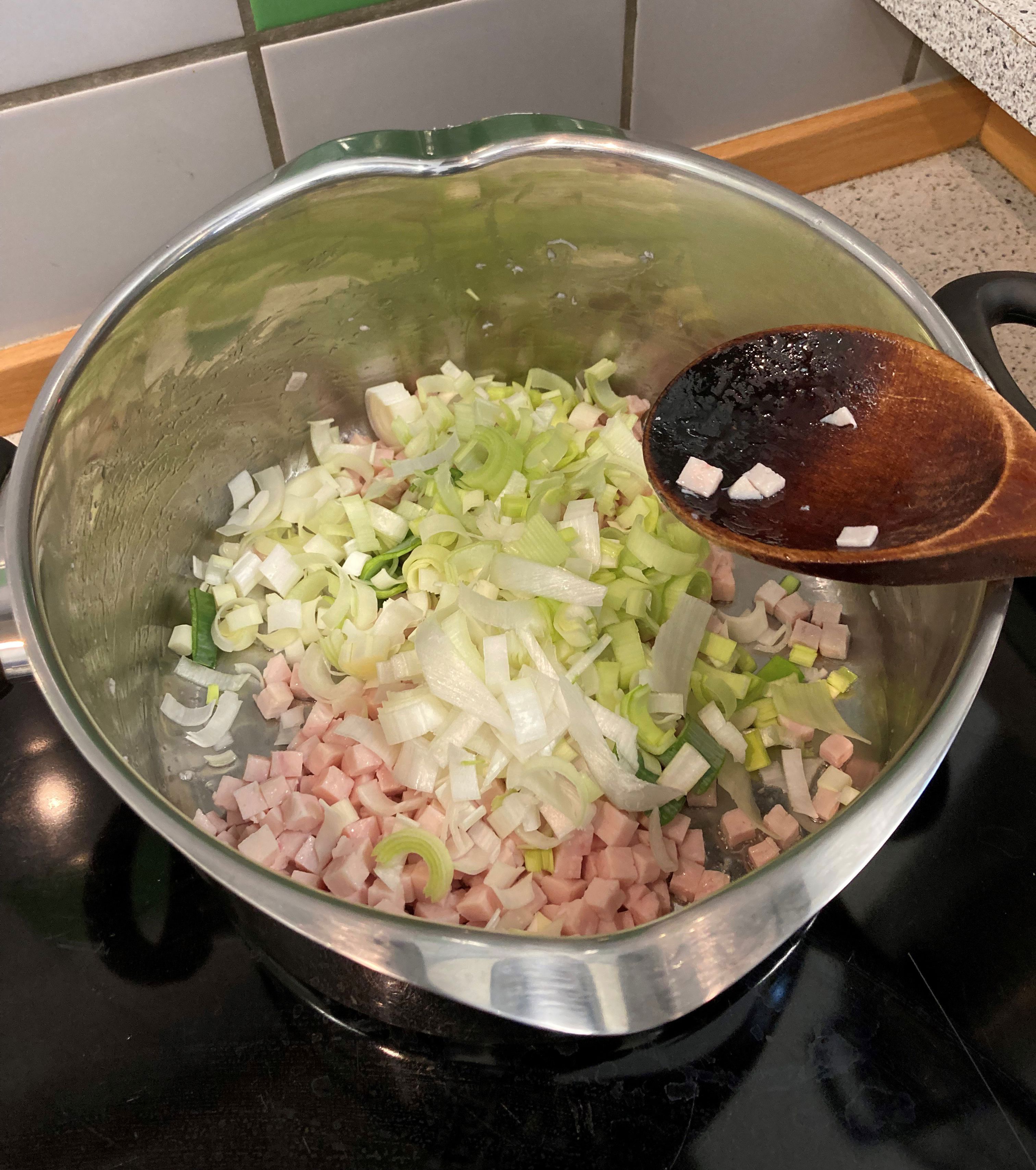 Nede i grydes ses kødet og porrerne, der bliver rørt i det med en grydeske af træ.