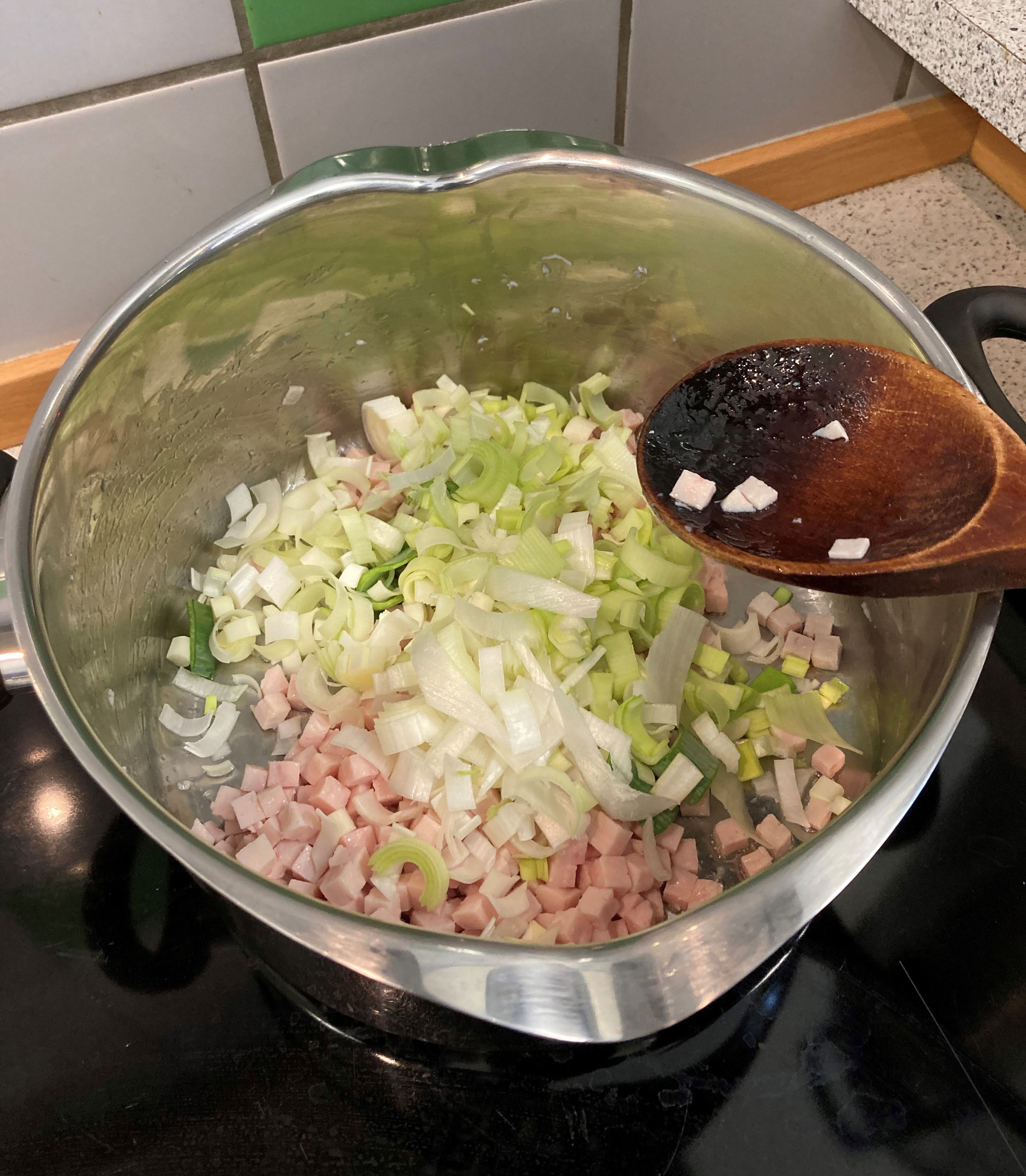 Nede i grydes ses kødet og porrerne, der bliver rørt i det med en grydeske af træ.