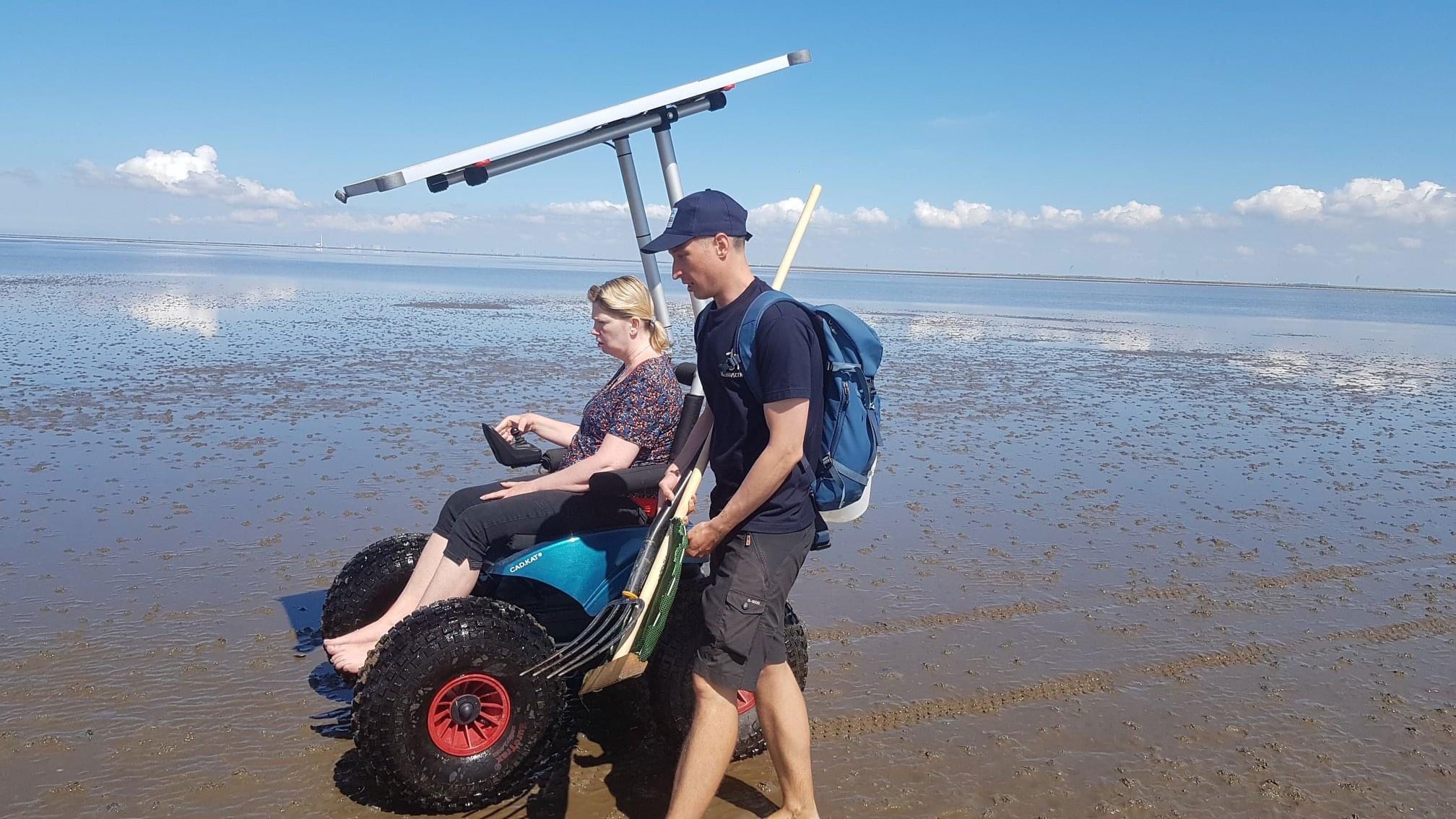Kørestolsbruger kører på stranden i vandkanten