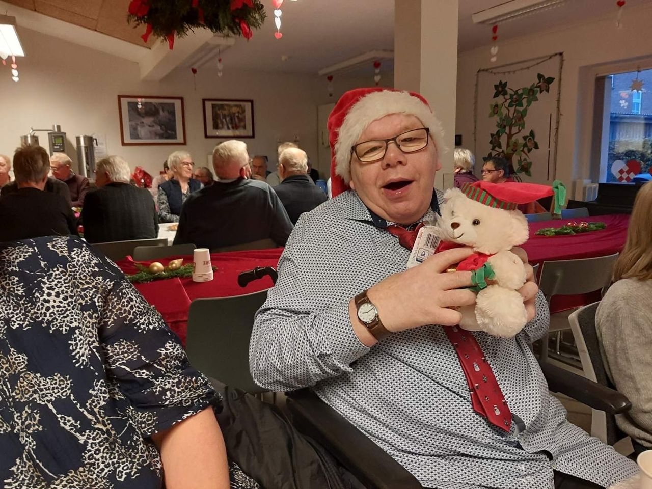 Borger sidder foran et juledækket bord. Borger har en nissehue på, og sidder med en julebamse i favnen.