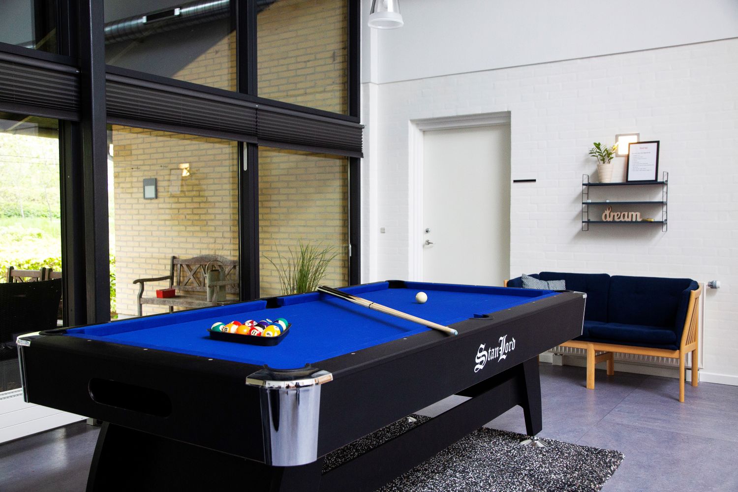 Billardbord sorte med blå dug ovenpå ligger billardkuglerne og to køer. det står op af et stort vinduesparti