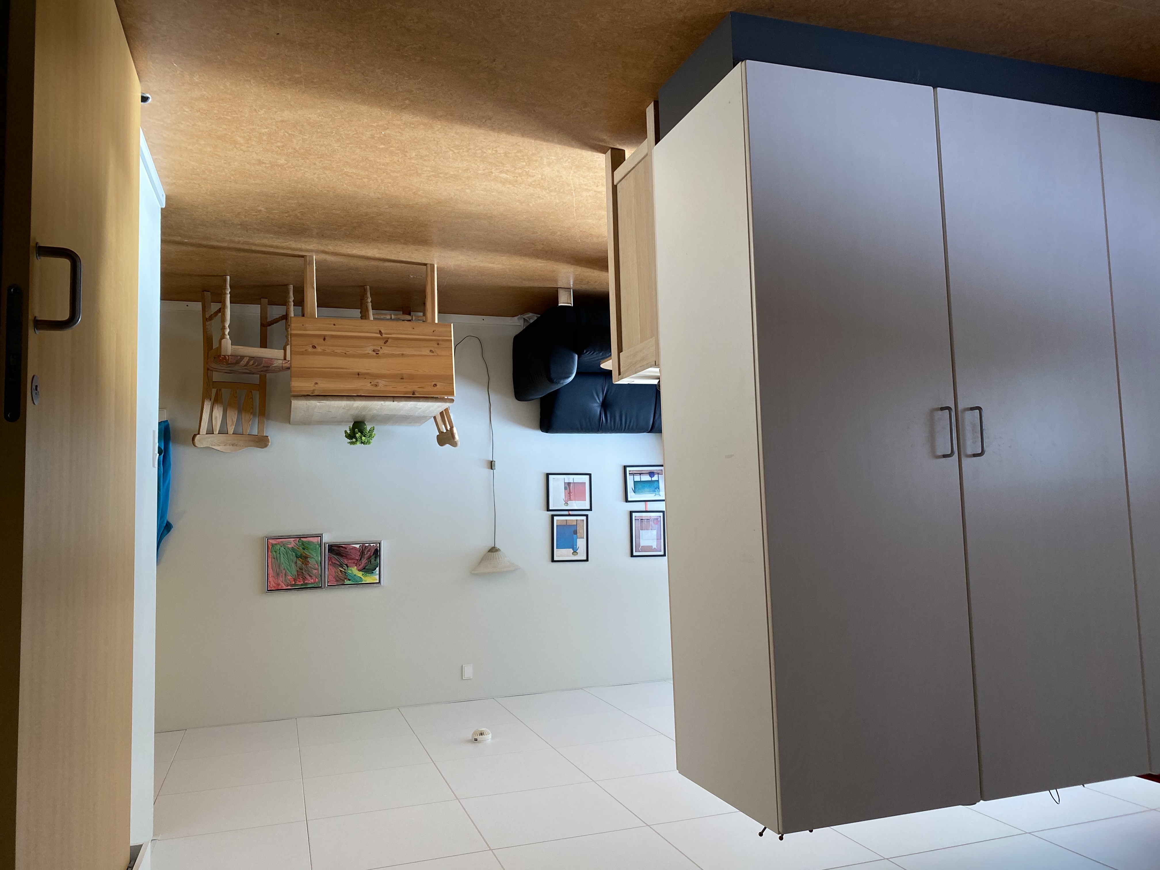 I en borgers lejlighed er der et spisebord med to stole. Der er en væg med skabe og en sofa. 