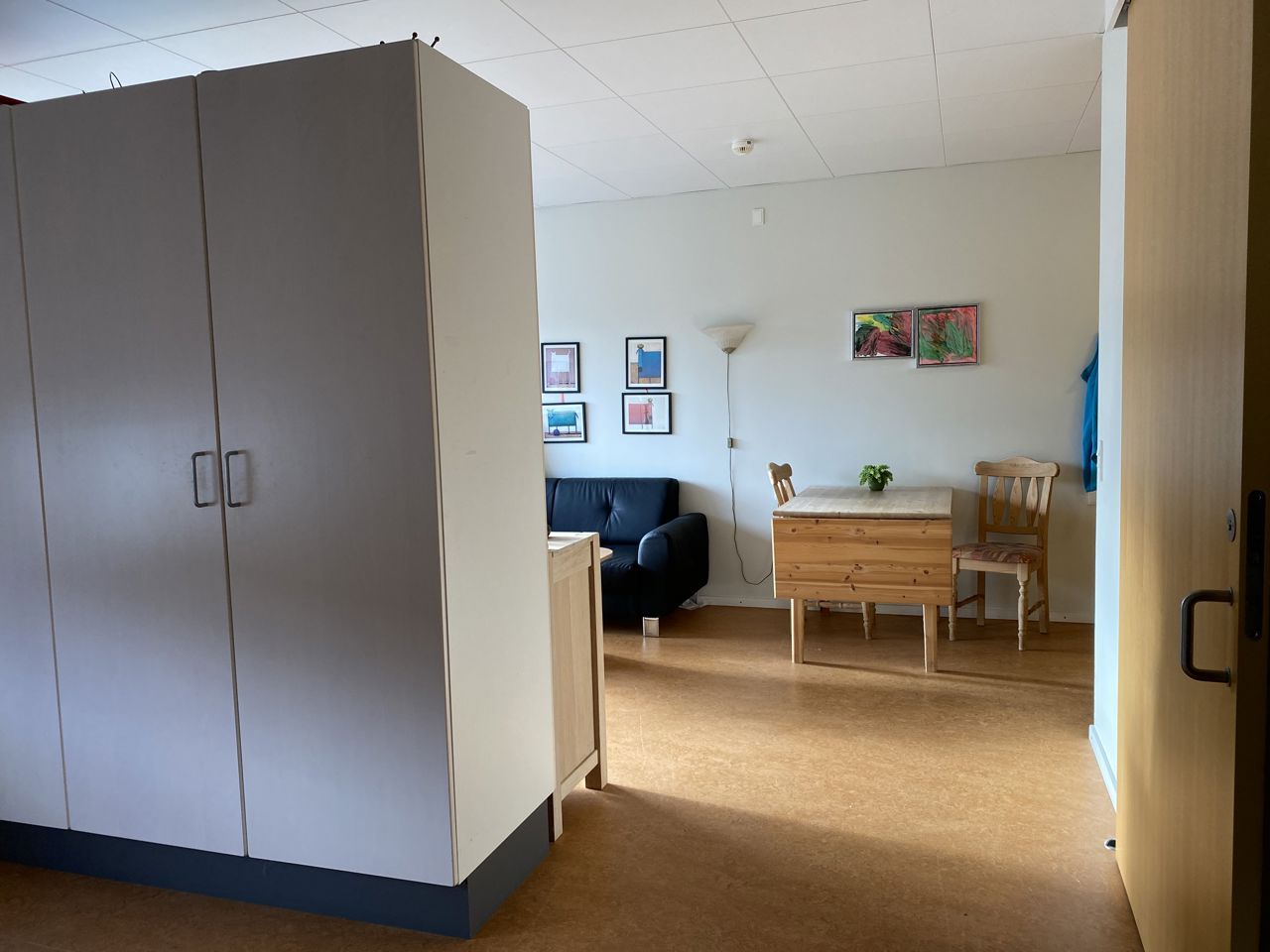 I en borgers lejlighed er der et spisebord med to stole. Der er en væg med skabe og en sofa.