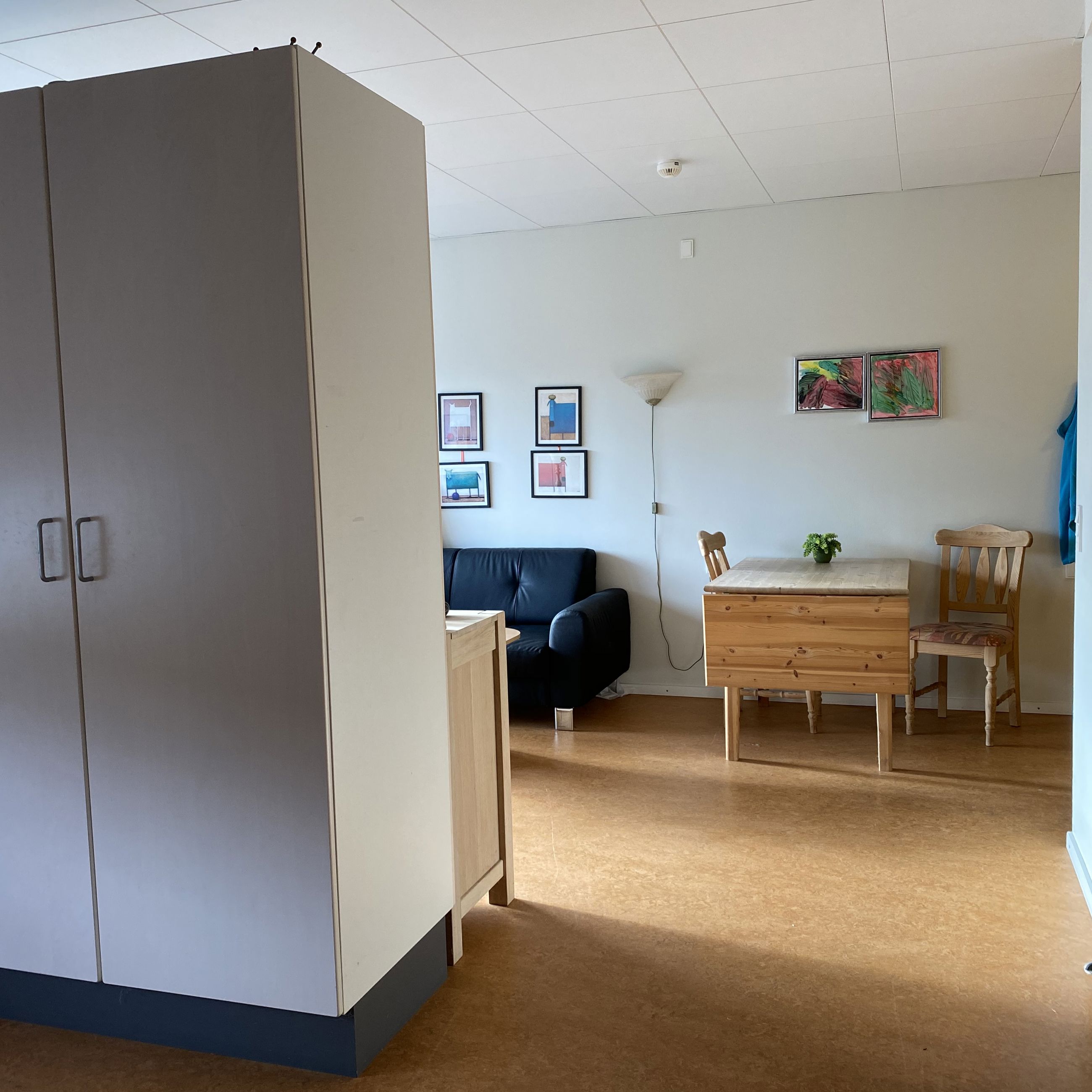 I en borgers lejlighed er der et spisebord med to stole. Der er en væg med skabe og en sofa.