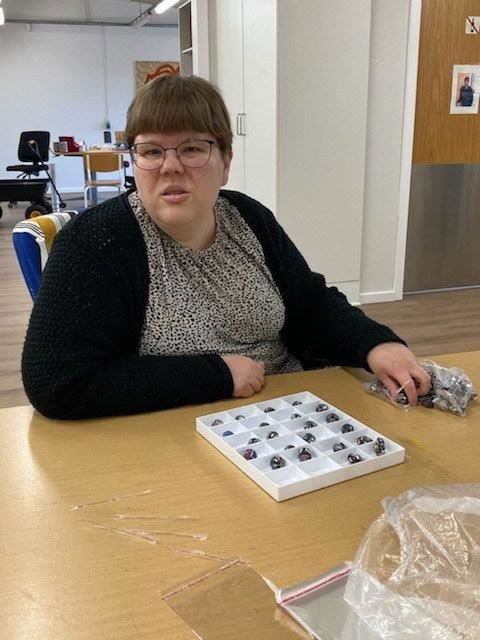 Borger sidder og pakker små metaldele i en æske hvor der er en masse små rum. Foran æsken ligger der også små lynlåsposer der kan pakkes varer i.