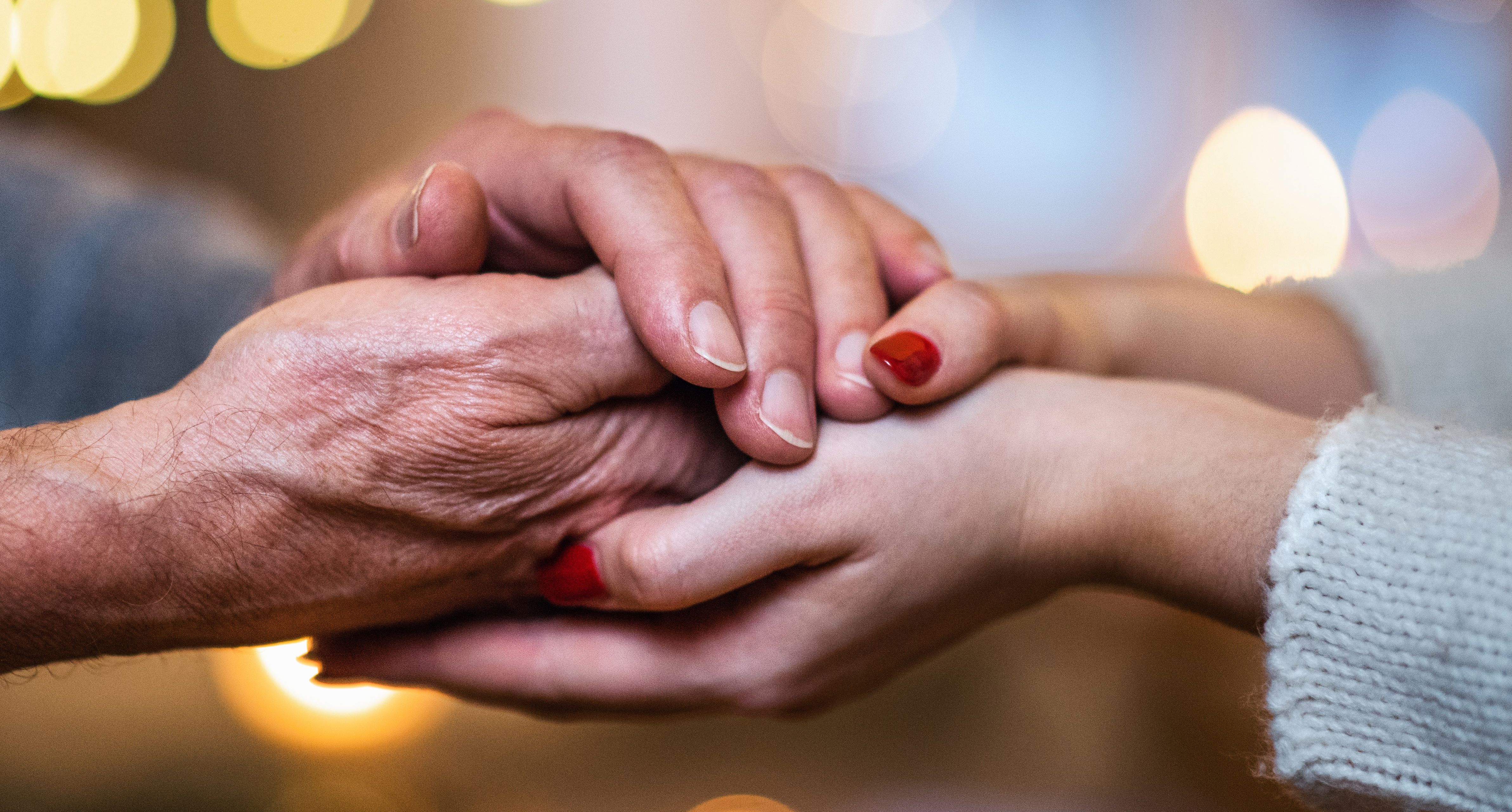 Billede af to personer der holder hinanden i hånden. Den ene person er ældre og den anden ung.