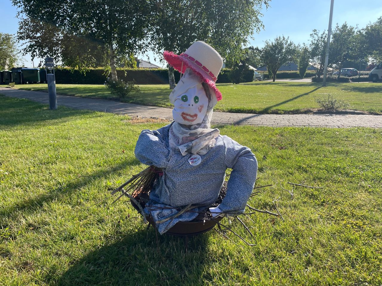 Heksen forfra, hun har en blå kjole på et tørklæde og på hovedet en stråhat.