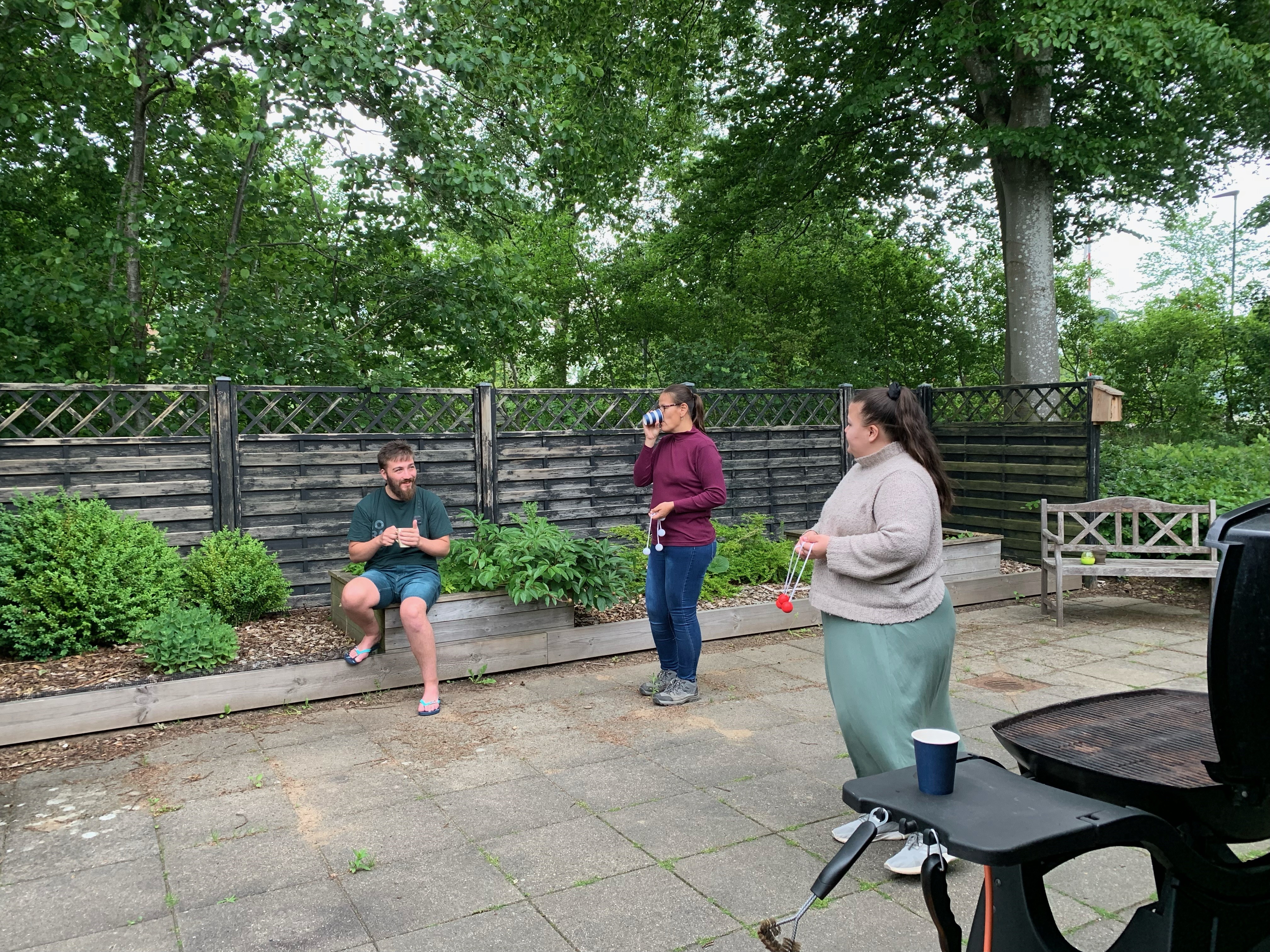 2 kvinder spiller stigegolf, i  baggrunden sidder der en mand og følger med mens han drikker en kop kaffe.