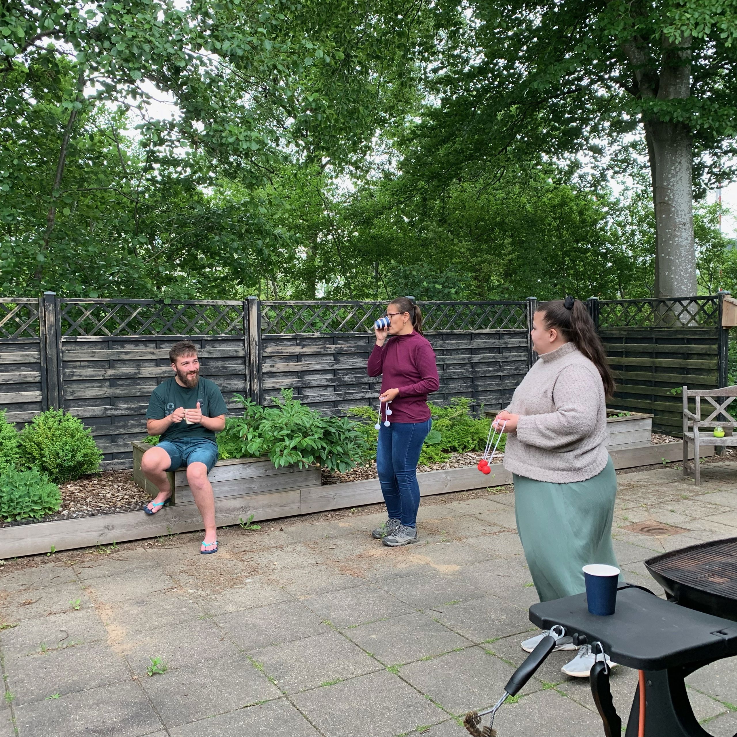 2 kvinder spiller stigegolf, i baggrunden sidder der en mand og følger med mens han drikker en kop kaffe.