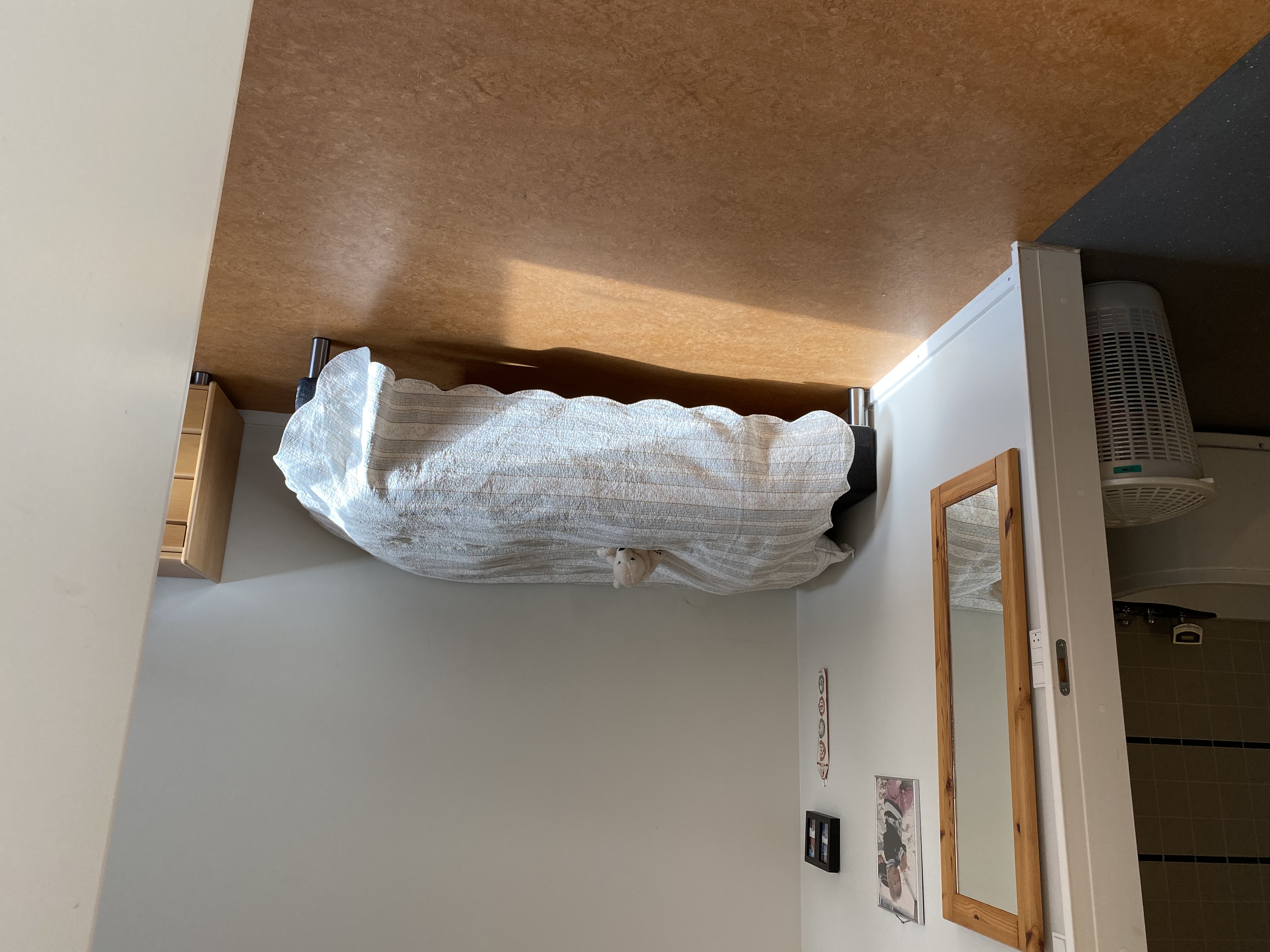 En borgers lejlighed hvor der er en seng. Gulvet er i lysebrune farver. Der hænget et langt spejl på væggen ind til toilettet. 