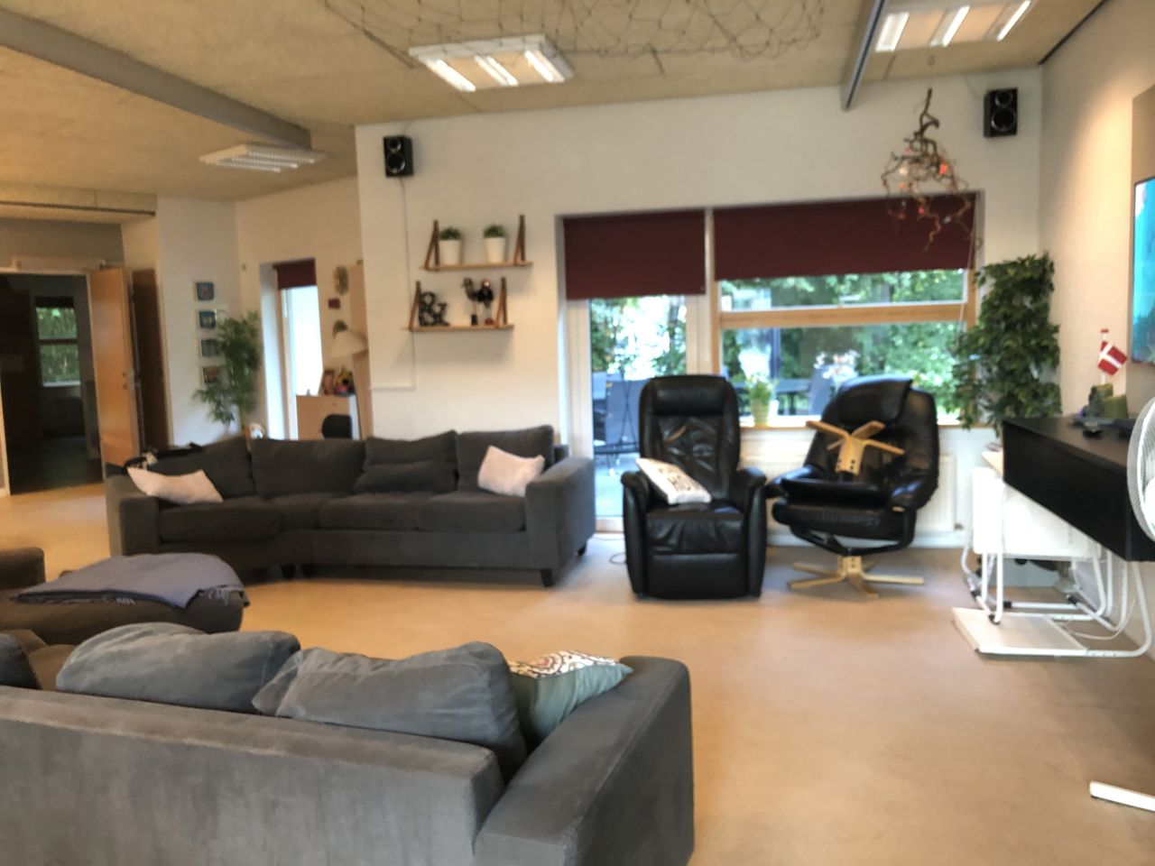 I opholdsrummet til venstre står der to sofaer overfor hinanden. Ved den ene sofa er der to læder lænestole. Gulvet er lyst laminatgulv. I enden af rummet er der et stort vindue og en terrassedør.