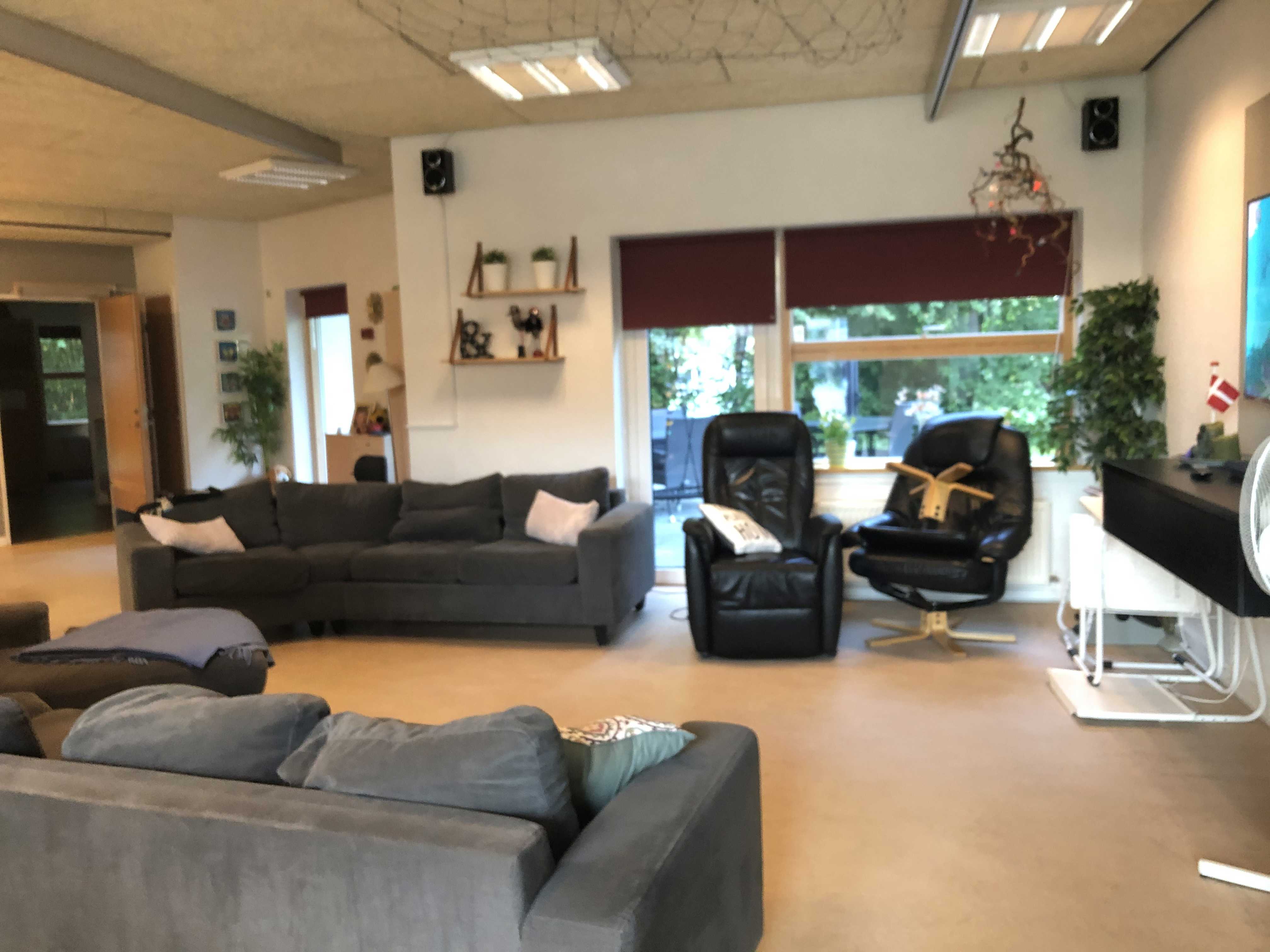 I opholdsrummet til venstre står der to sofaer overfor hinanden. Ved den ene sofa er der to læder lænestole. Gulvet er lyst laminatgulv. I enden af rummet er der et stort vindue og en terrassedør.