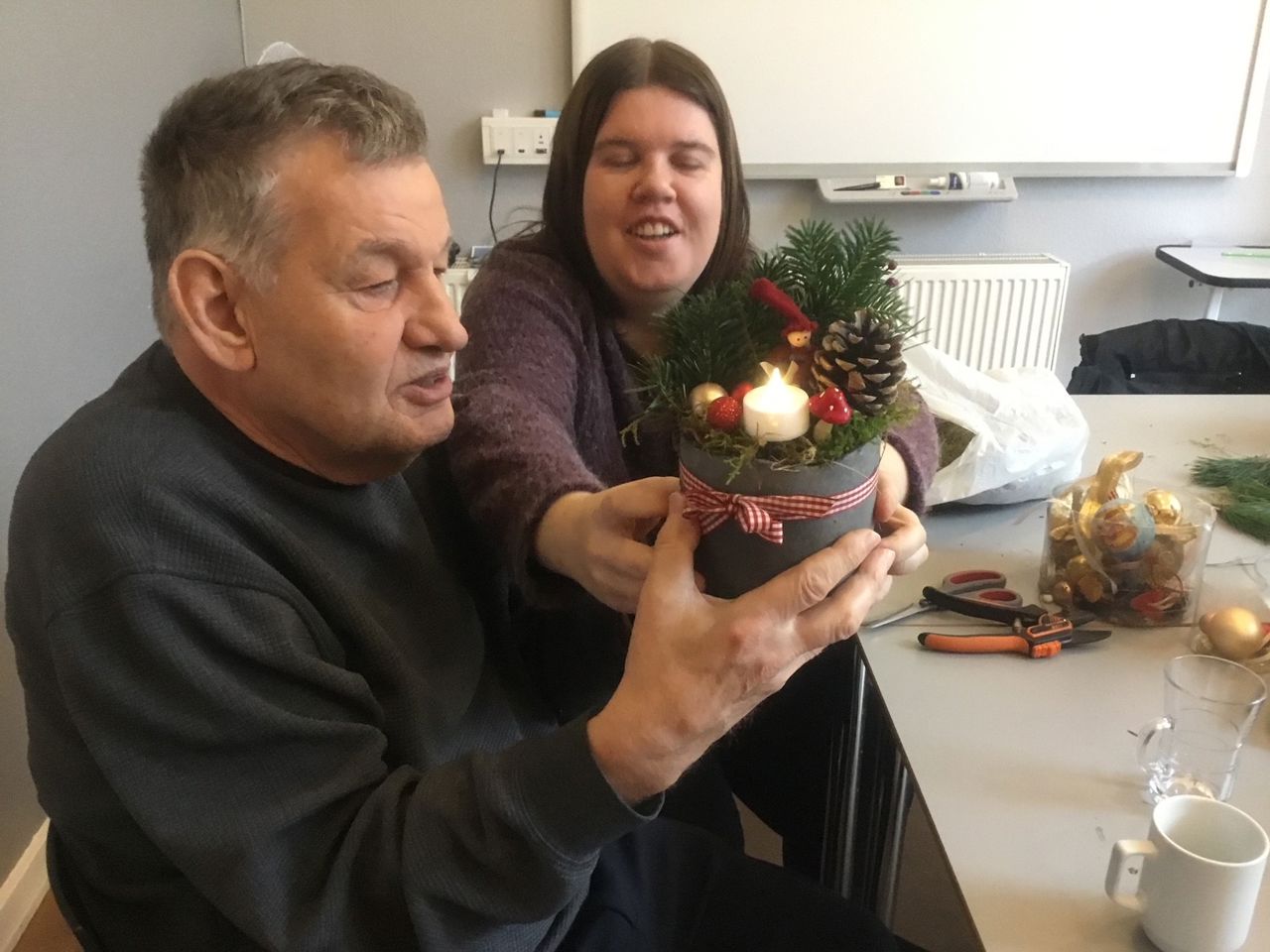 To borgere viser en flot juledekoration frem, på bordet ved dem ligger forskellige ting der er blevet brugt til at fremstille den her juledekoration.