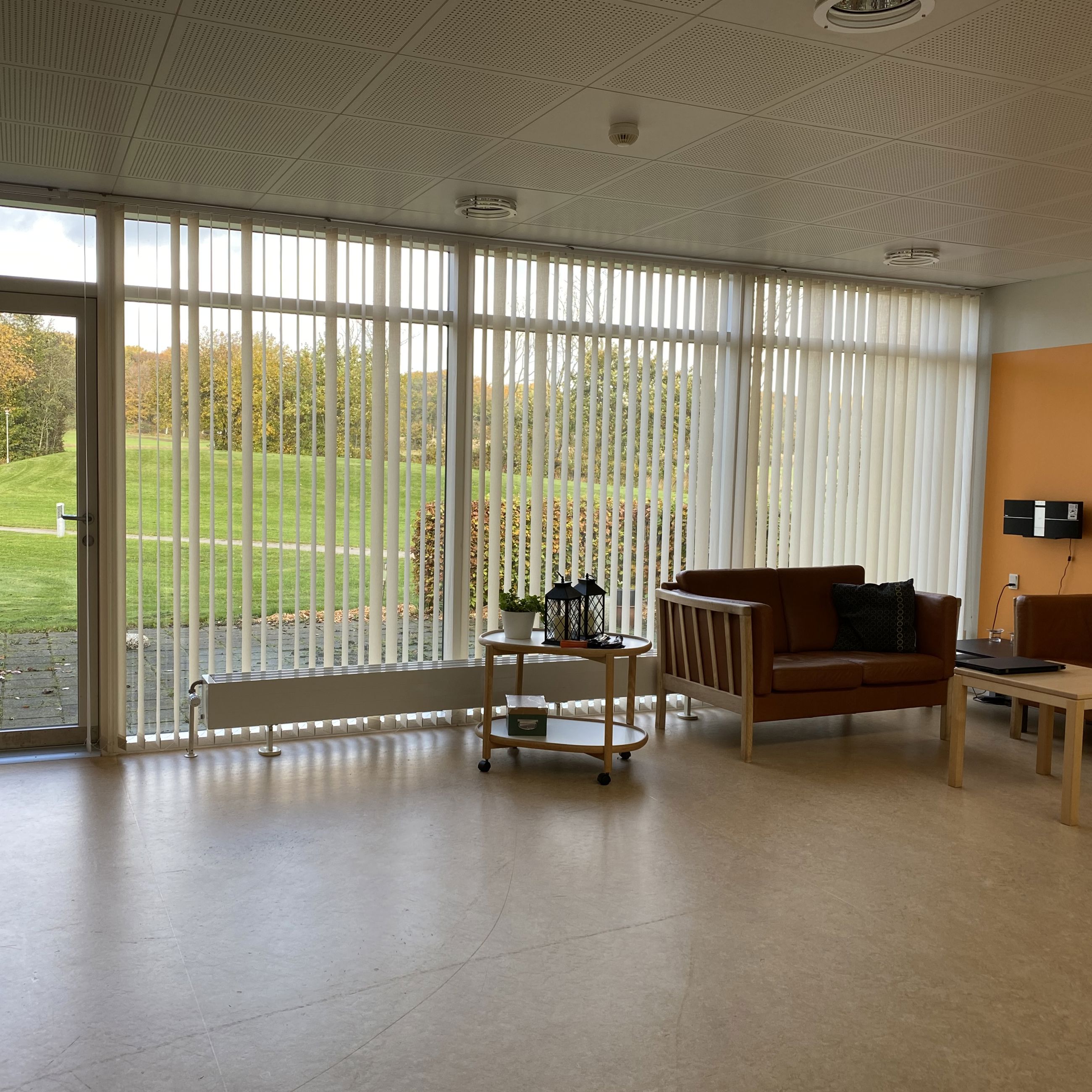 Opholdsstuen på Æblevej 1 er der to brune læder sofaer og et lille firkantet bord. Den ene væg i stuen er malet orange. Gulvet er lysebrunt.