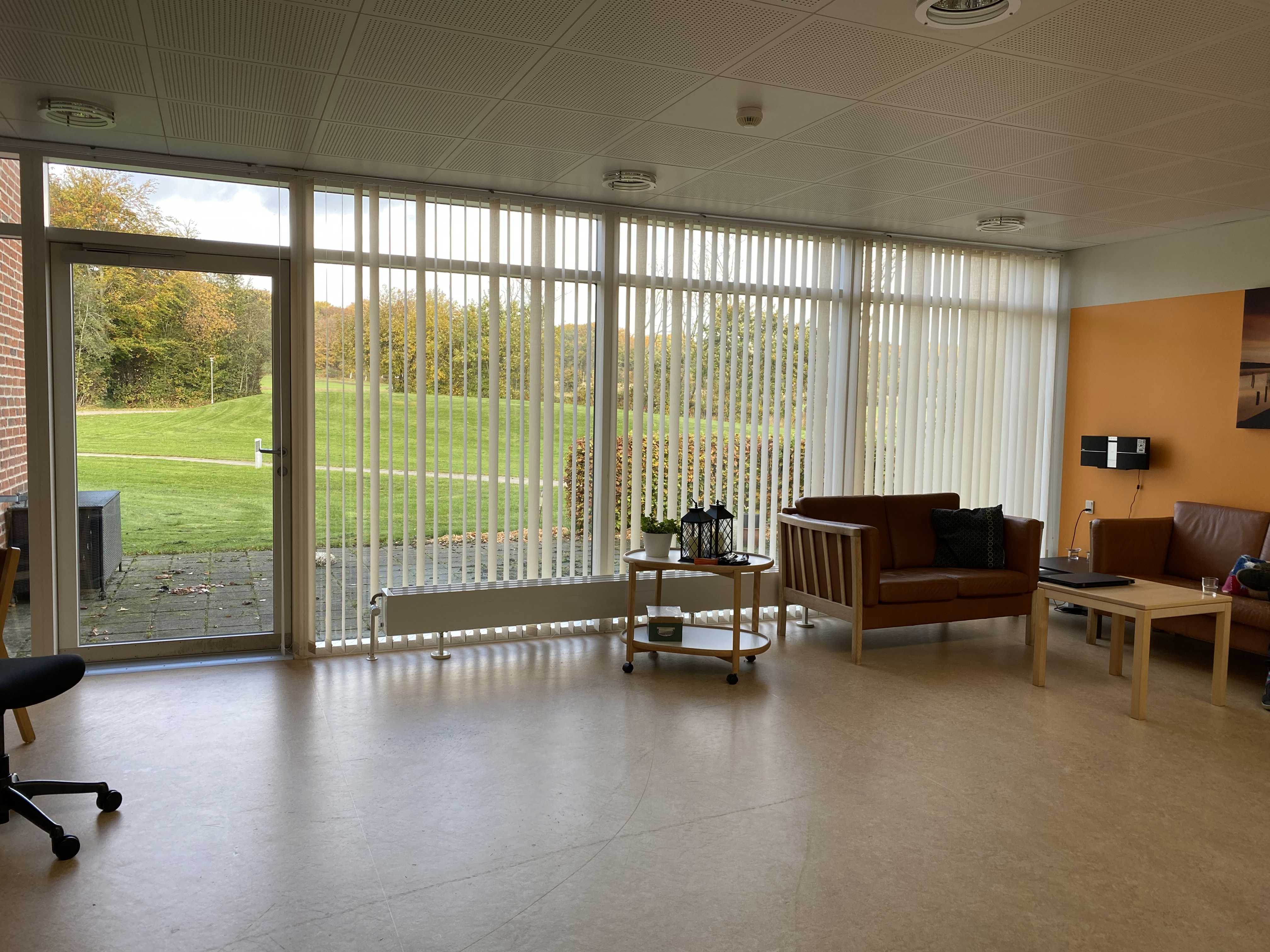 Opholdsstuen på Æblevej 1 er der to brune læder sofaer og et lille firkantet bord. Den ene væg i stuen er malet orange. Gulvet er lysebrunt.