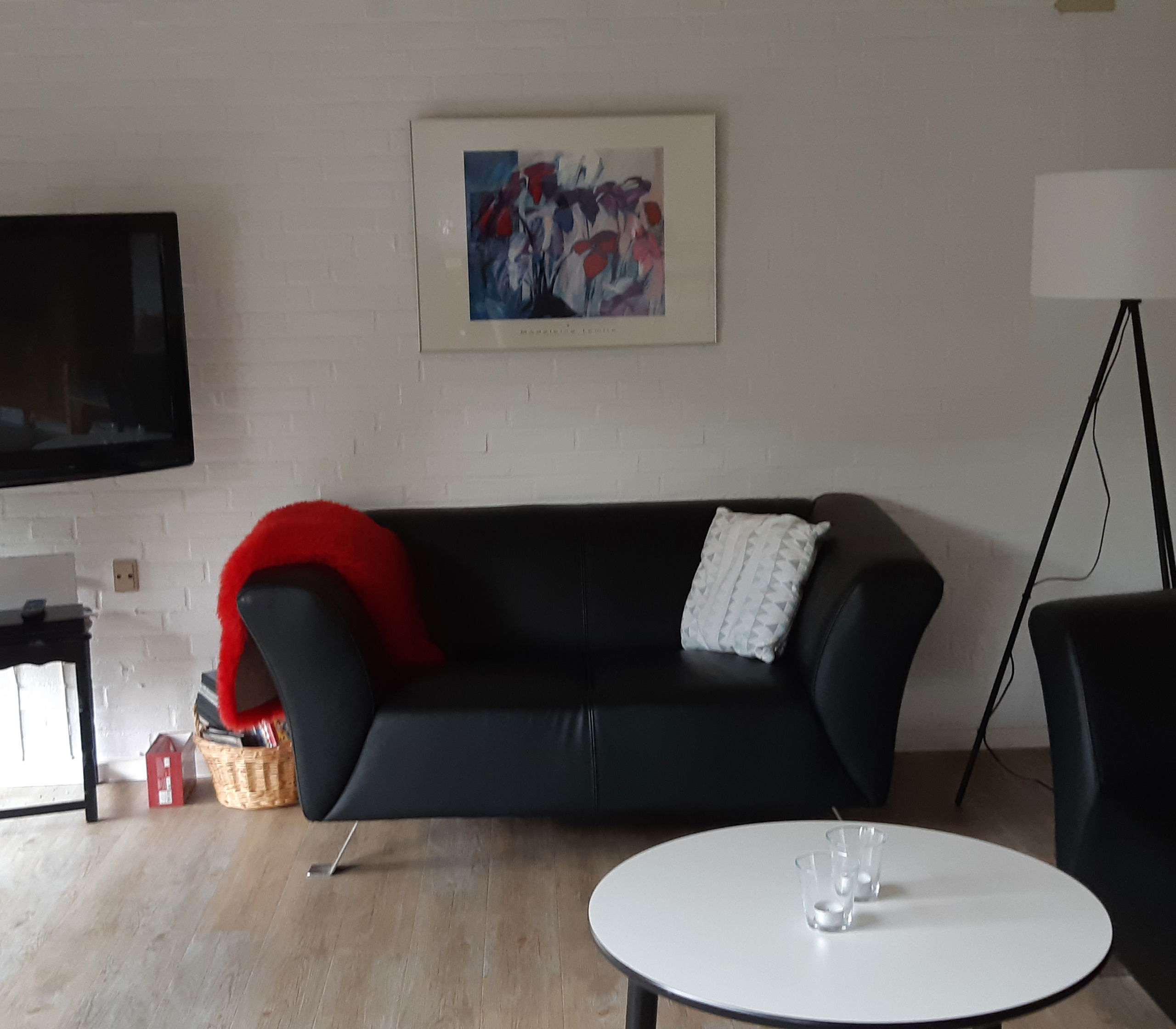 Opholdsstue med to lædersofaer, et rundt bord og et tv. I hjærnet er der er høj standerlampe med hvid lampeskærm.