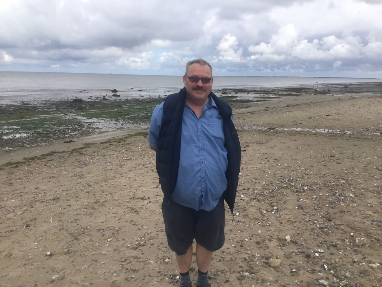 En borger står ved stranden, i baggrunden kan man se vandet og noget tang i vandkanten.