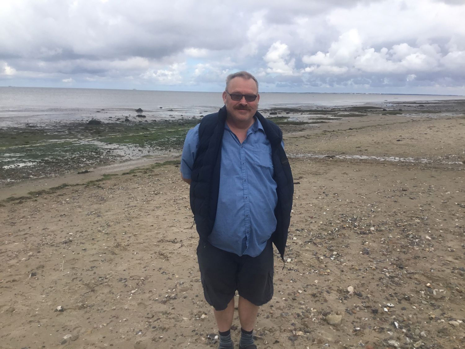 En borger står ved stranden, i baggrunden kan man se vandet og noget tang i vandkanten.