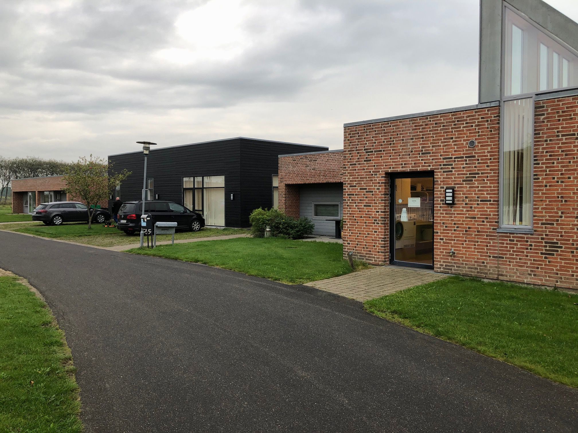 Æblevej 2 udefra. Bygninger er af røde mursten, og træ der er malet sort. Foran bygningerne er der en sti der fører ind til indgangen til Æblevej . Midt i billedet står der en grå lygtepæl.