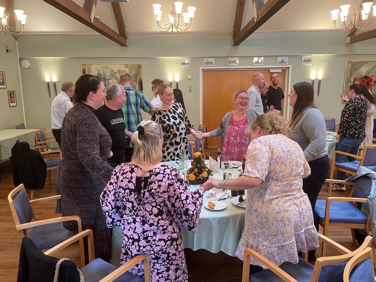 Alle dansker kædedans ved bordene og alle griner, de har alle fint festtøj på