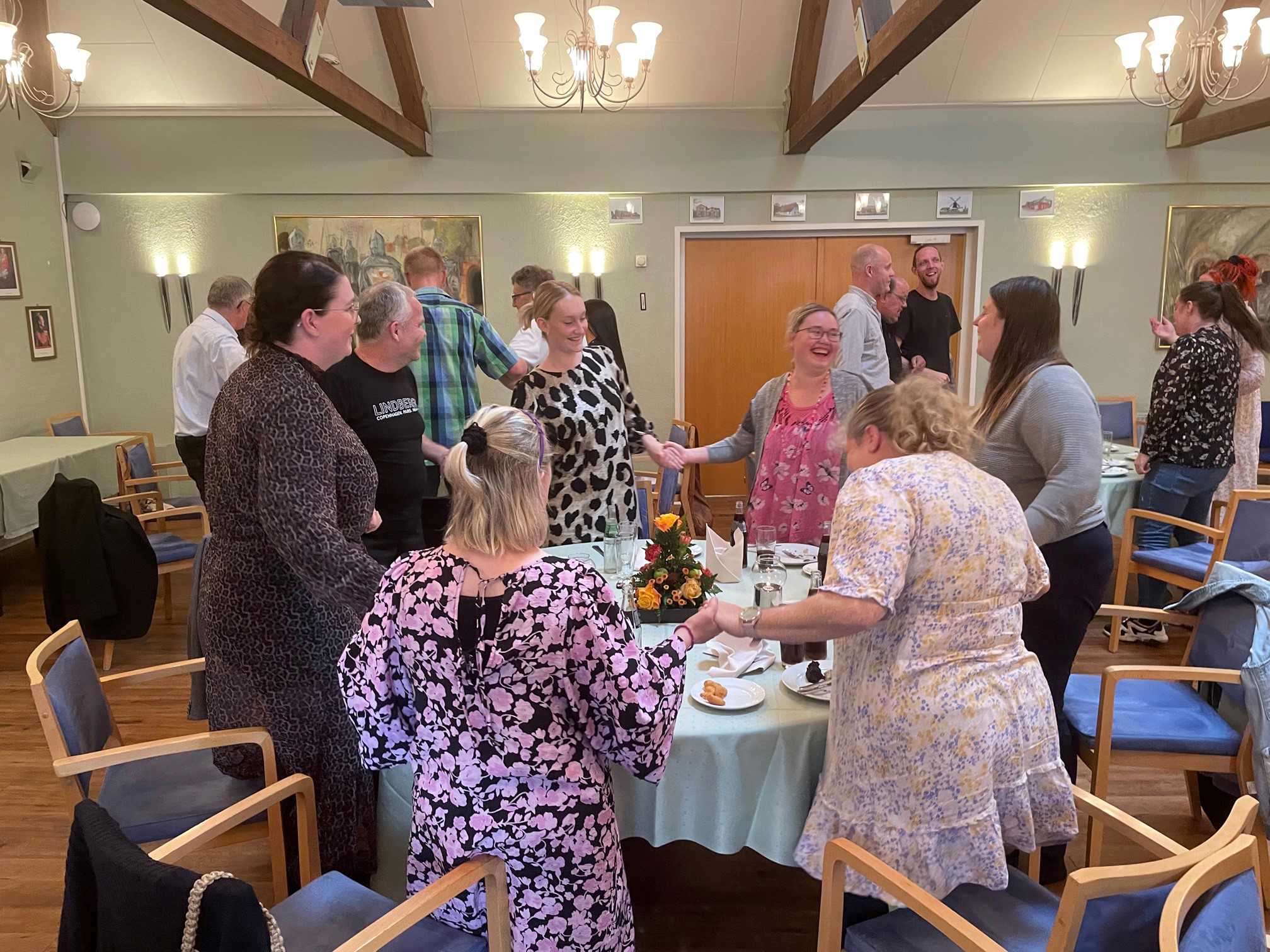 Alle dansker kædedans ved bordene og alle griner, de har alle fint festtøj på