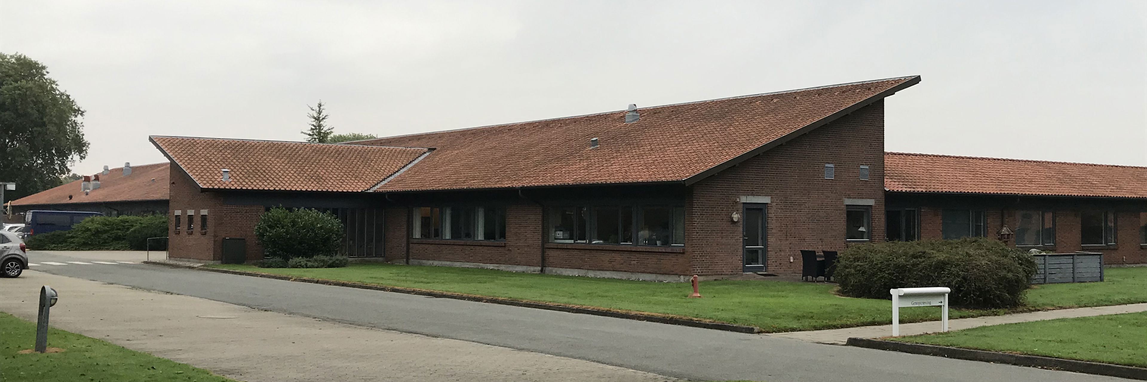 En lang indkørsel med Klosterparken i baggrunden i røde sten og rød tegltag.
