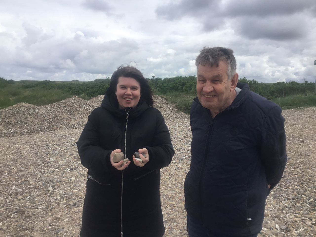 To borgere står ved en strand med mange sten, den ene har hænderne fulde af de mange sten hun har samlet.