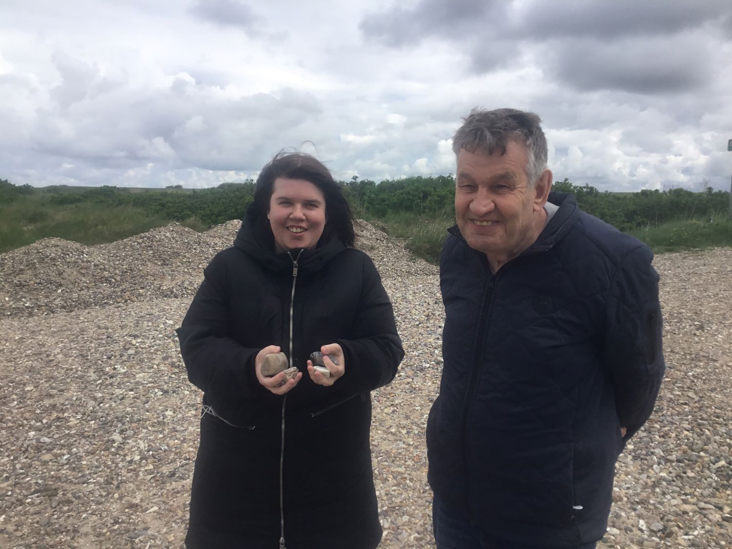 To borgere står ved en strand med mange sten, den ene har hænderne fulde af de mange sten hun har samlet.