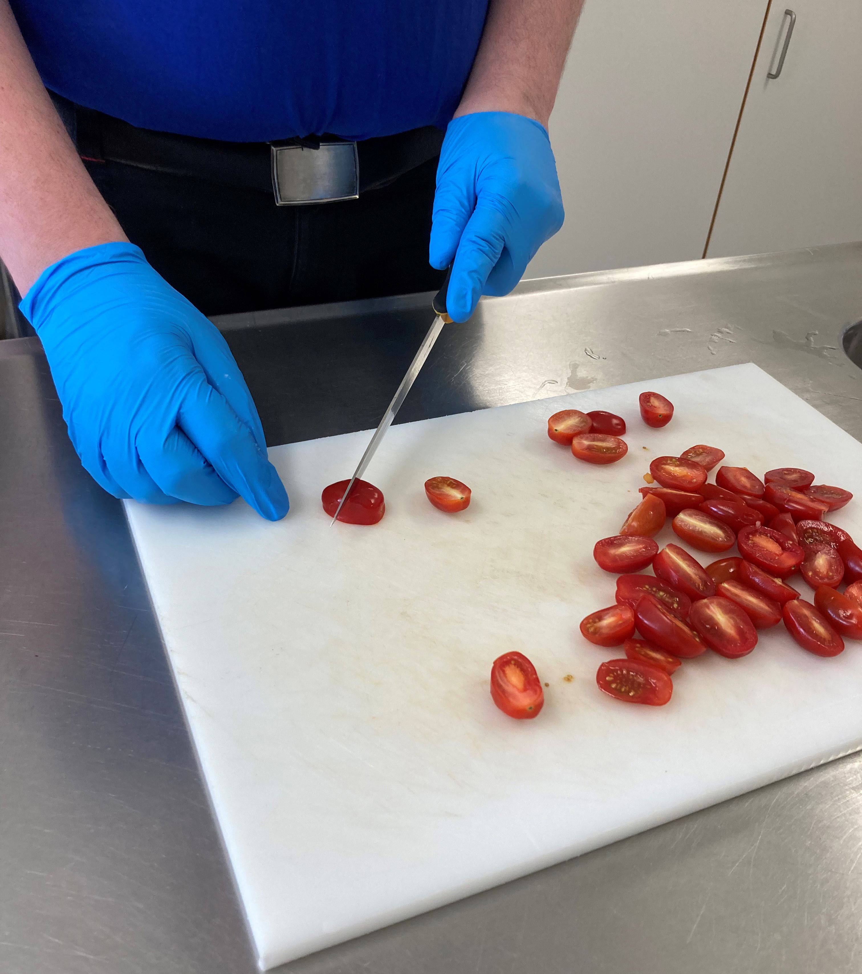 En borger skærer cherrytomater i halve på et hvidt skærebræt.
