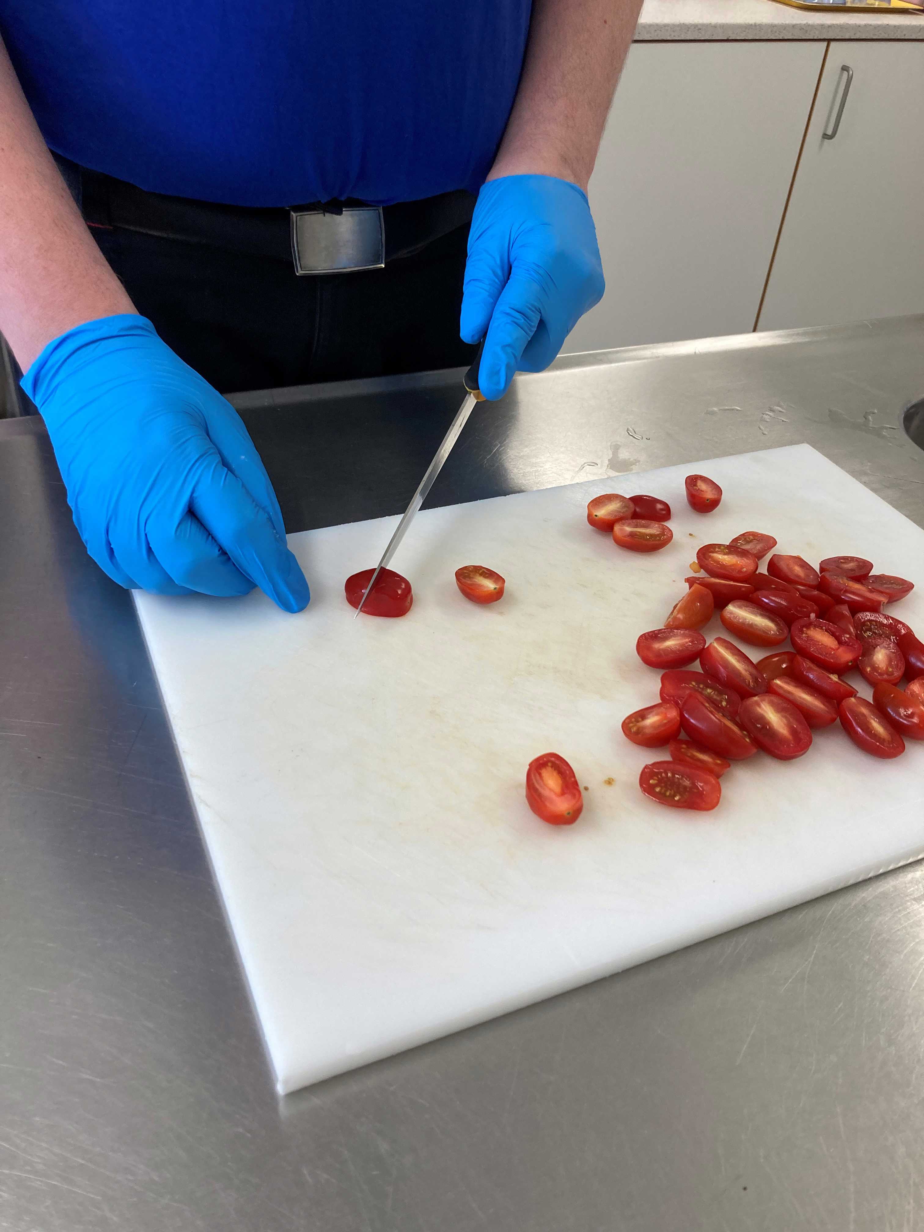 En borger skærer cherrytomater i halve på et hvidt skærebræt.