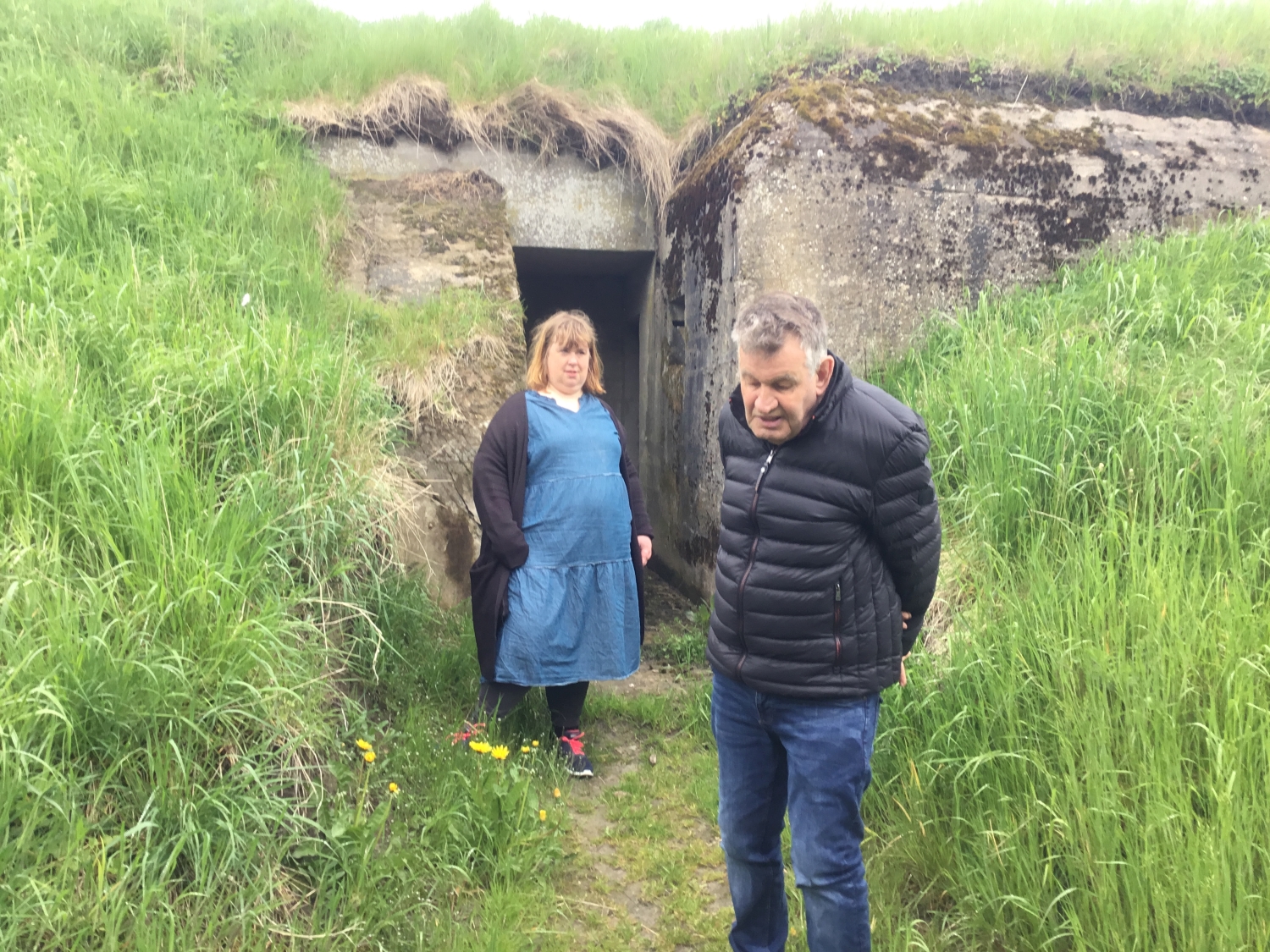 To borgere står ved indgang til en bunker, på hver side er der frodige skråninger ned mod indgangen til bunkeren.