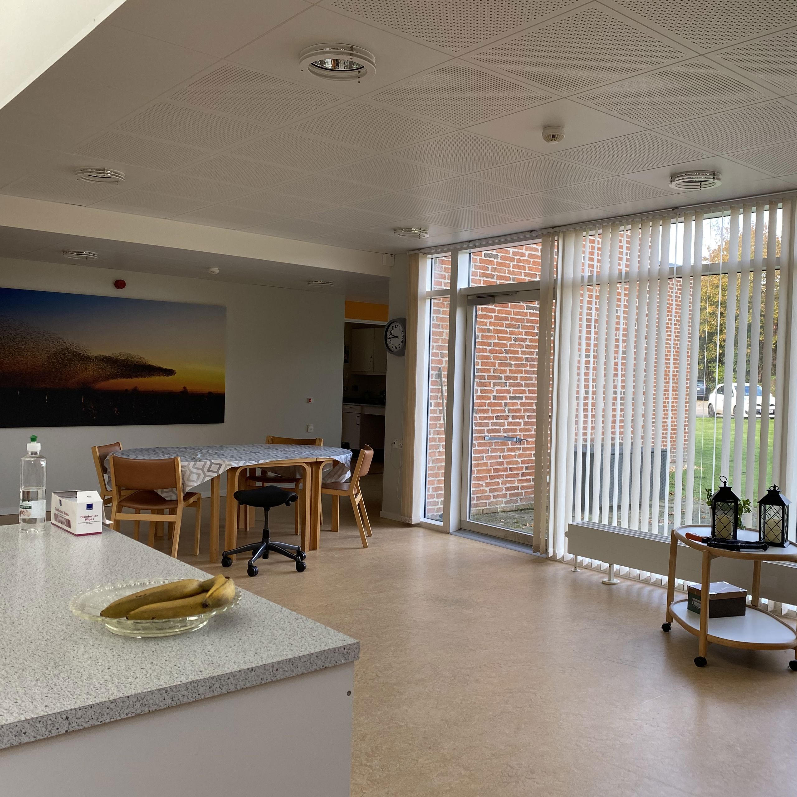 I opholdstuen er der et rundt bord med fire stole med rygløn og en stol med hjul. Henne ved det store vinduesparti er der et lille rullebord med nogle lanterner på.