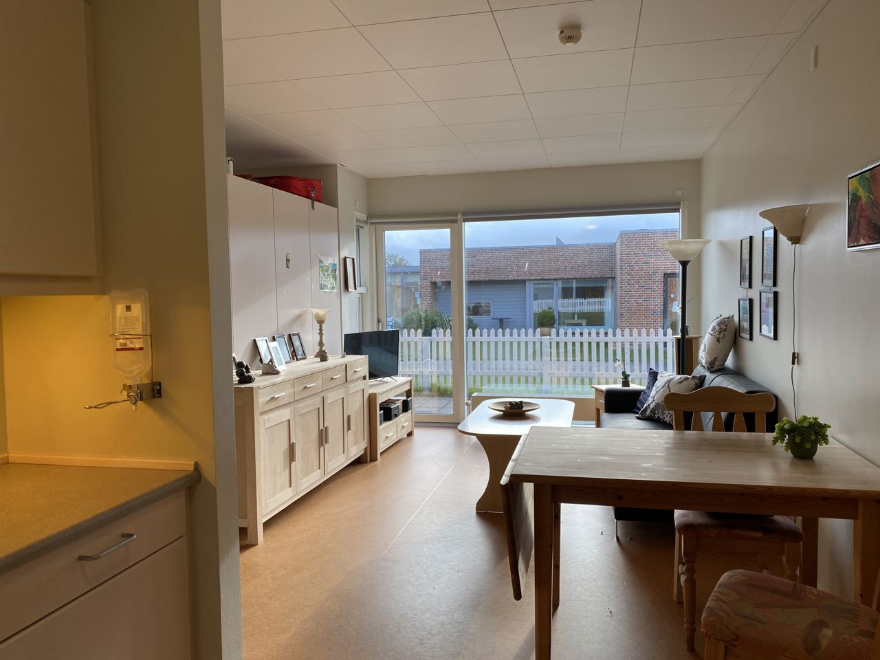 Inde i en borgers lejlighed er der en sofa og et sofabord. I lejligheden der en skænk og et tv bord. I lejligheden er der også et spisebord og et lille thekøkken.