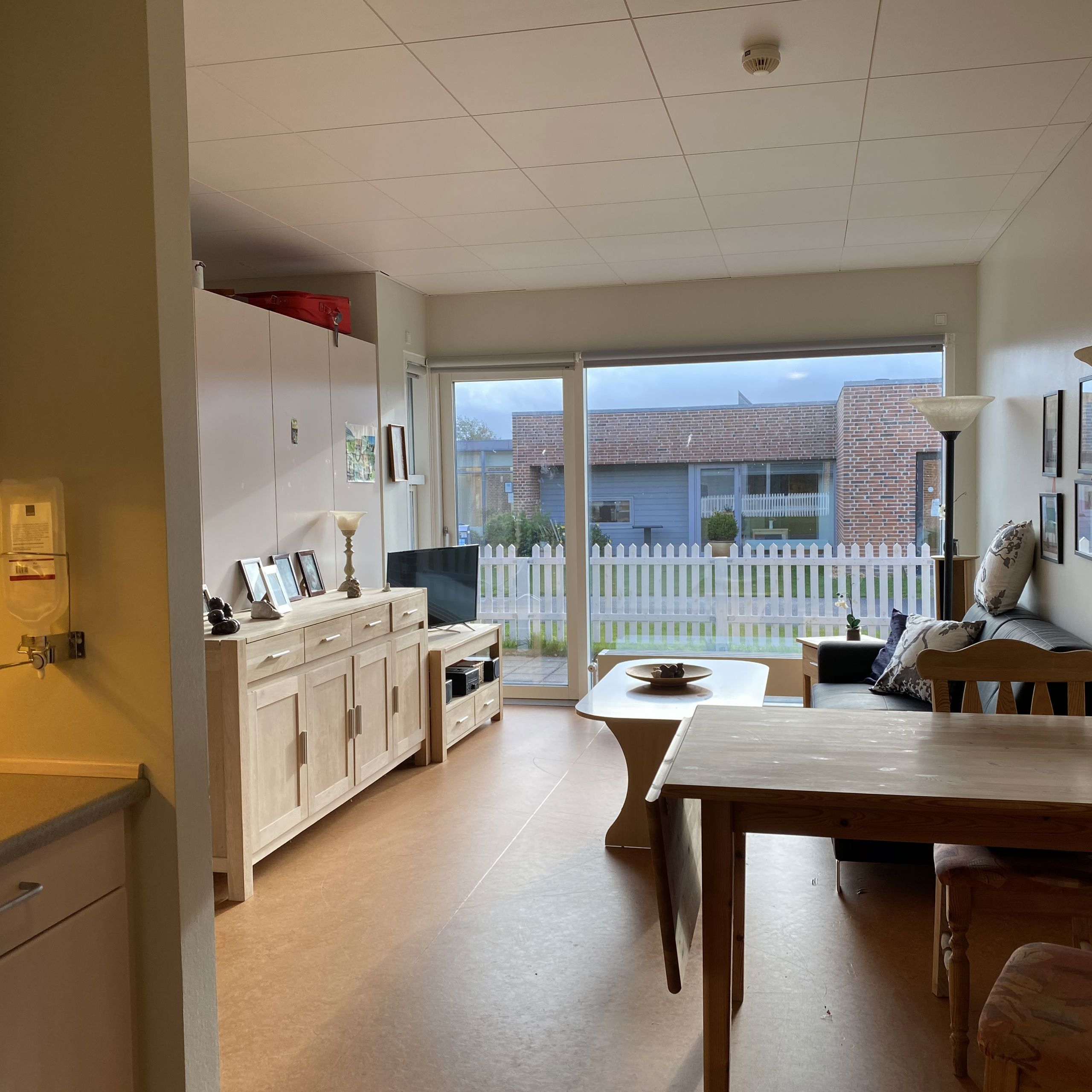 Inde i en borgers lejlighed er der en sofa og et sofabord. I lejligheden der en skænk og et tv bord. I lejligheden er der også et spisebord og et lille thekøkken.