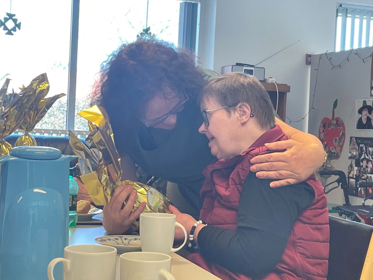 En borger får et påskeæg og et kram på bordet foran står der flere påskeæg og der sidder nogle borgere ved bordet