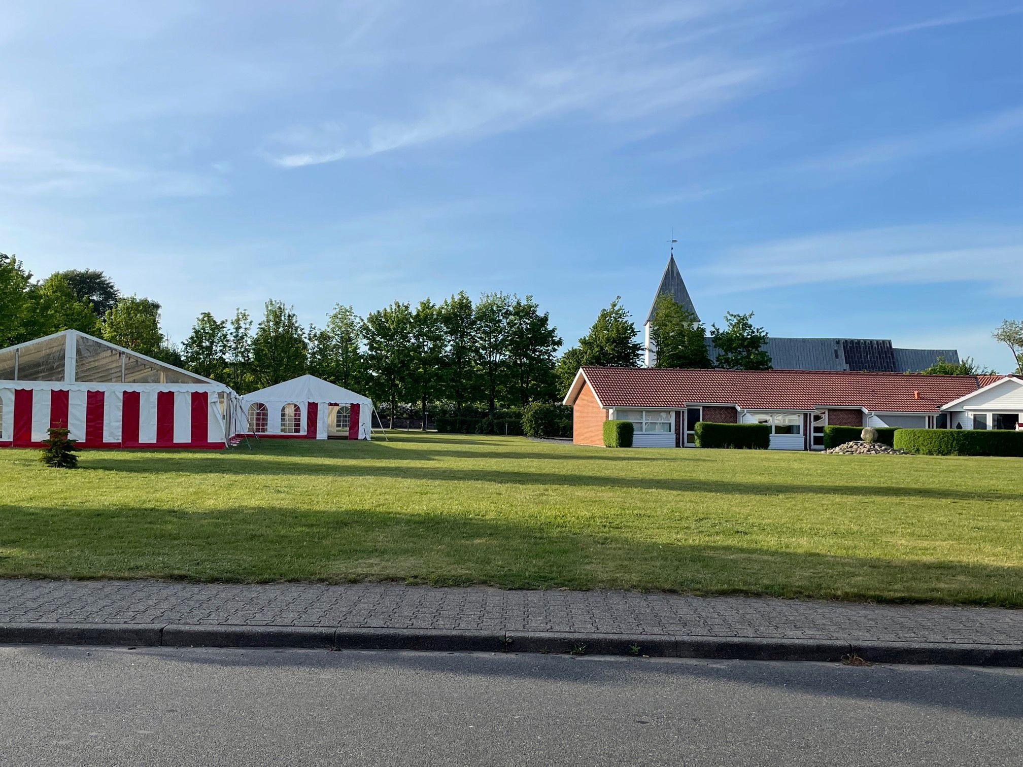 Billede af Lobæk parken med Løgumgårde kirke i baggrunden og på den grønne plads foran er står der 2 rød - hvide stribede telte.