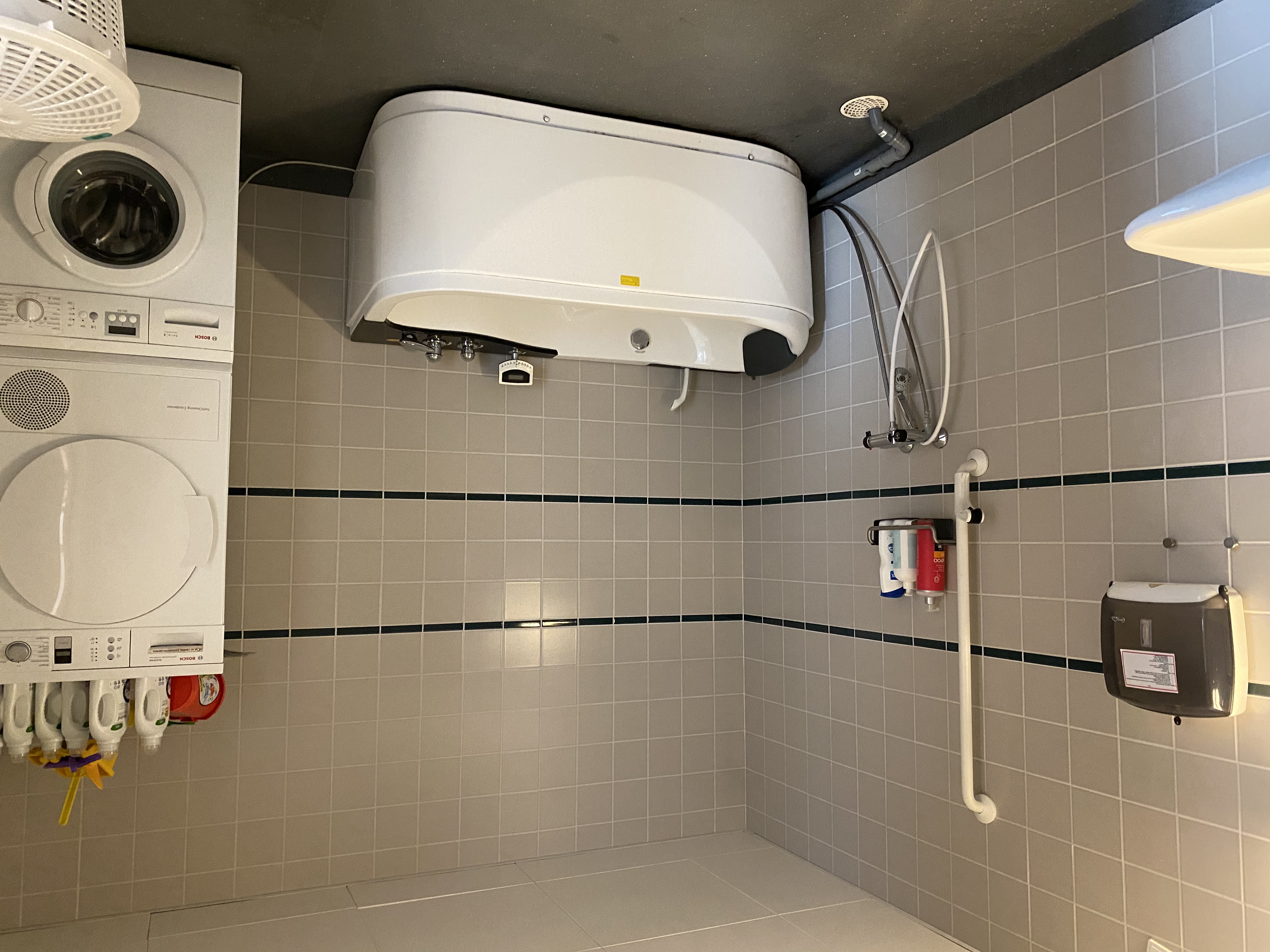 Badeværelset i en borgers lejlighed. Der er et spabad. I højre side af badeværelset er der en vaskemaskine og der står en tørretumbler ovenpå. 