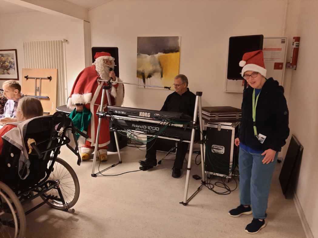 Julemanden står og giver et nummer, der sidder en mand ved et keyboard og spiller. I forgrunden står der en borger og danser.